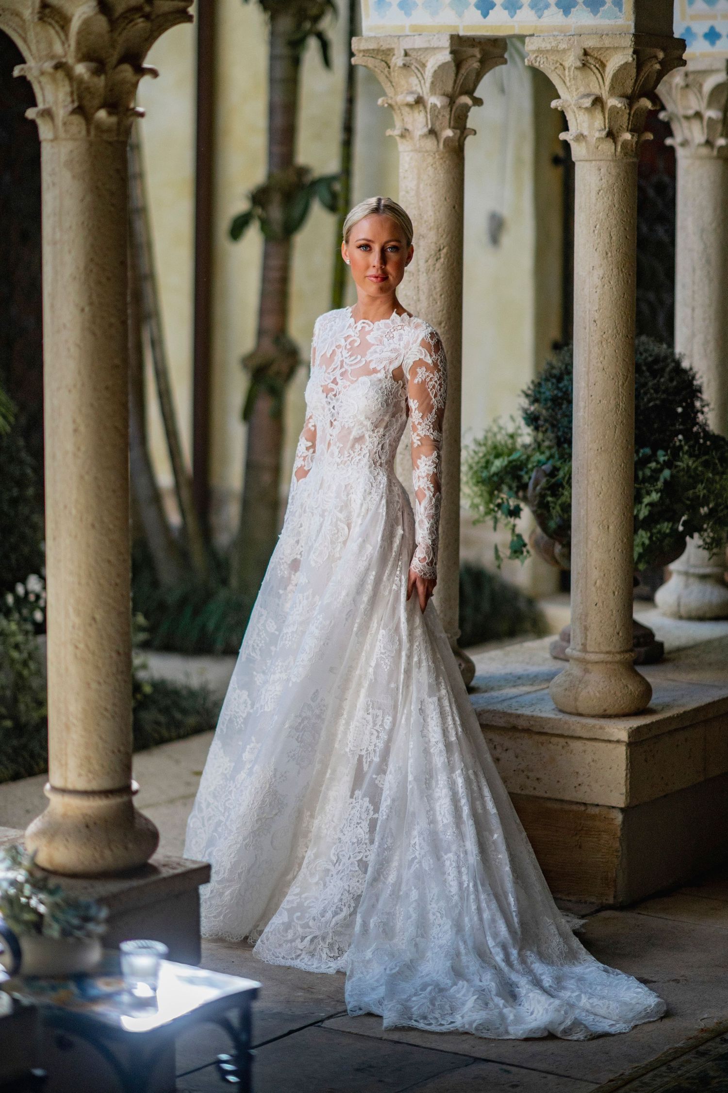 An elegant lace wedding gown with long sleeves photographed in a columned courtyard.