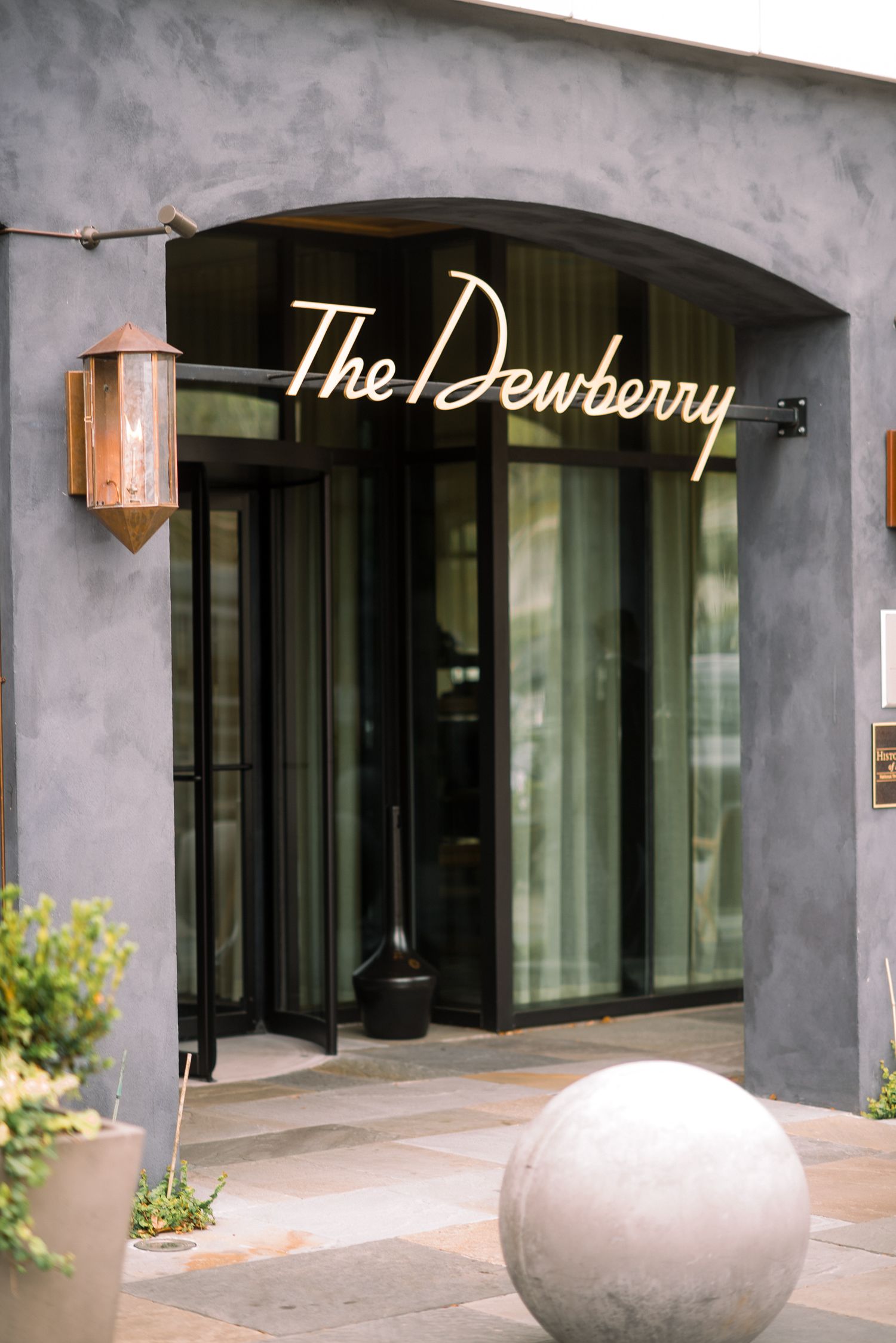Modern apartment building entrance with concrete walls, black-framed windows, and 'The Dewberry' signage illuminated.