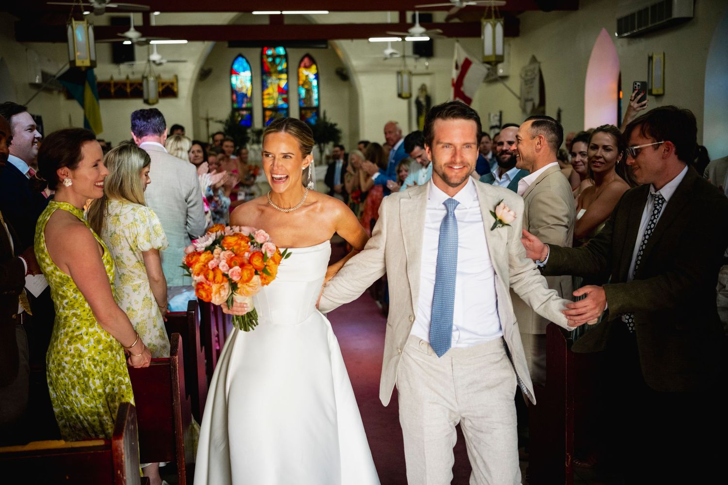 Wedding celebration in a church with guests lining the aisle as couple exits.