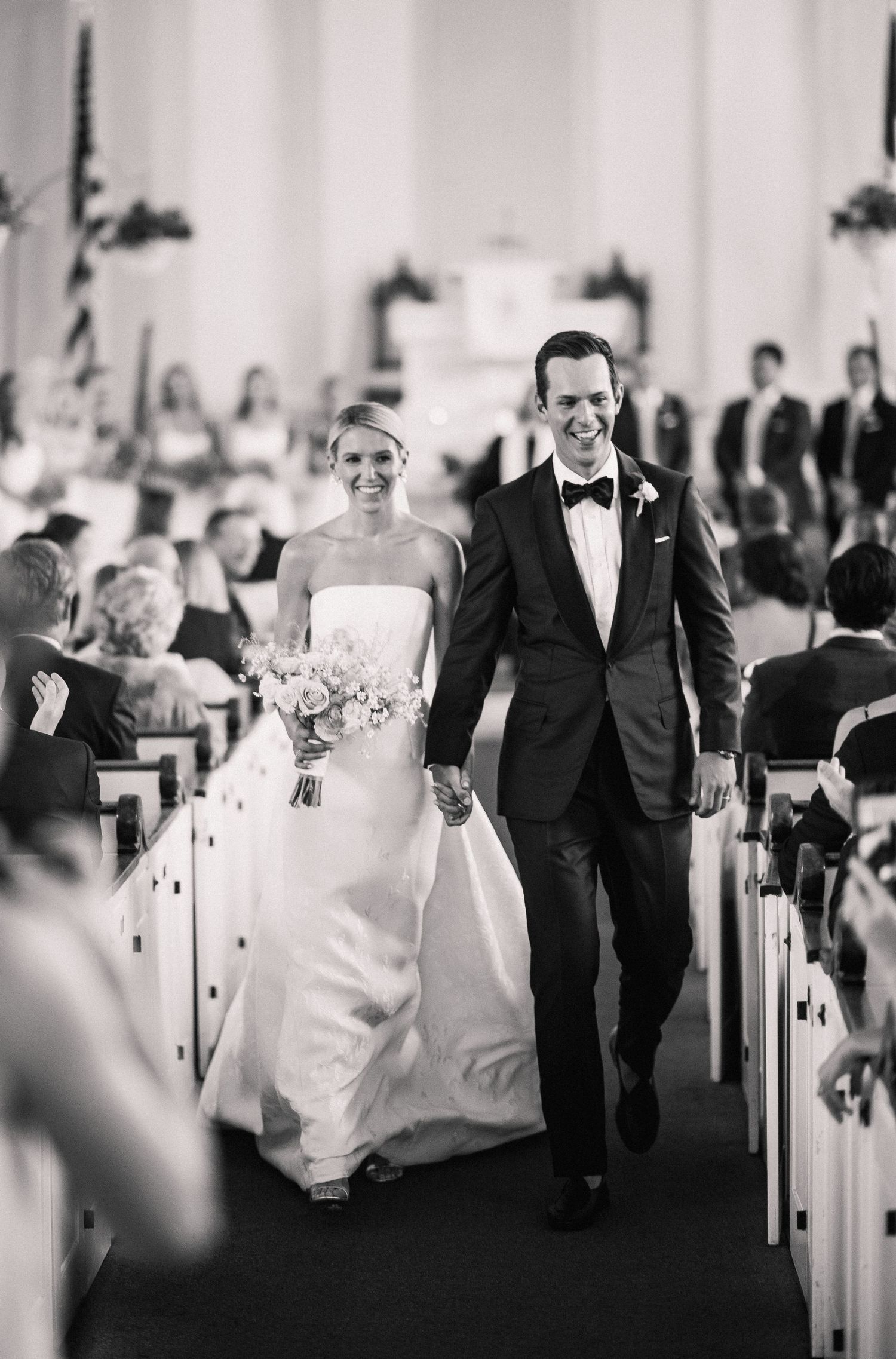 Black and white photo of newlyweds walking down church aisle after wedding ceremony.