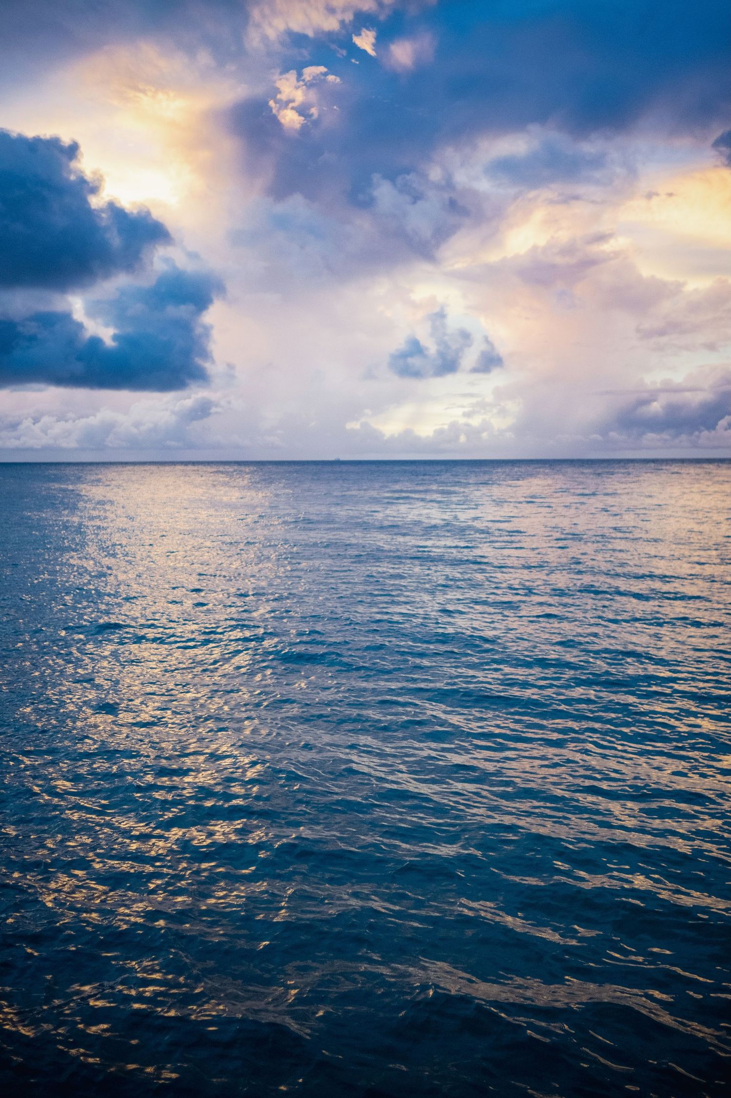 Dramatic sunset over calm ocean waters with vibrant purple and blue clouds reflecting on the rippling surface.