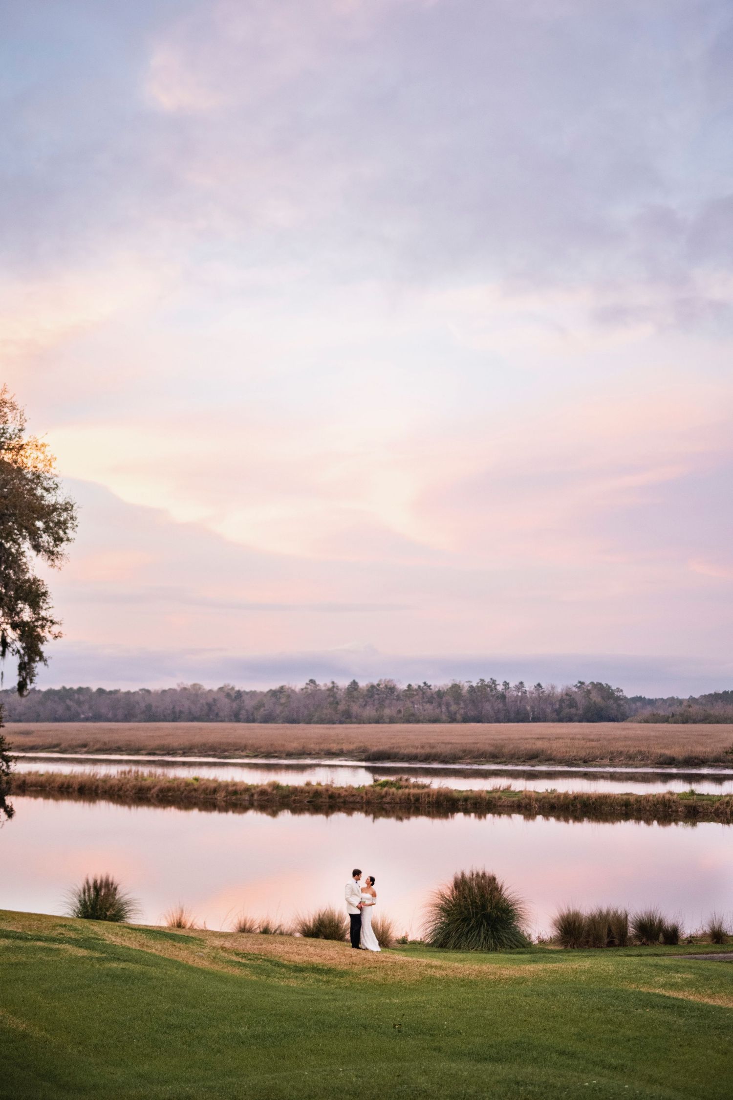 A peaceful marsh landscape at sunset with soft pink clouds reflecting on still waters.