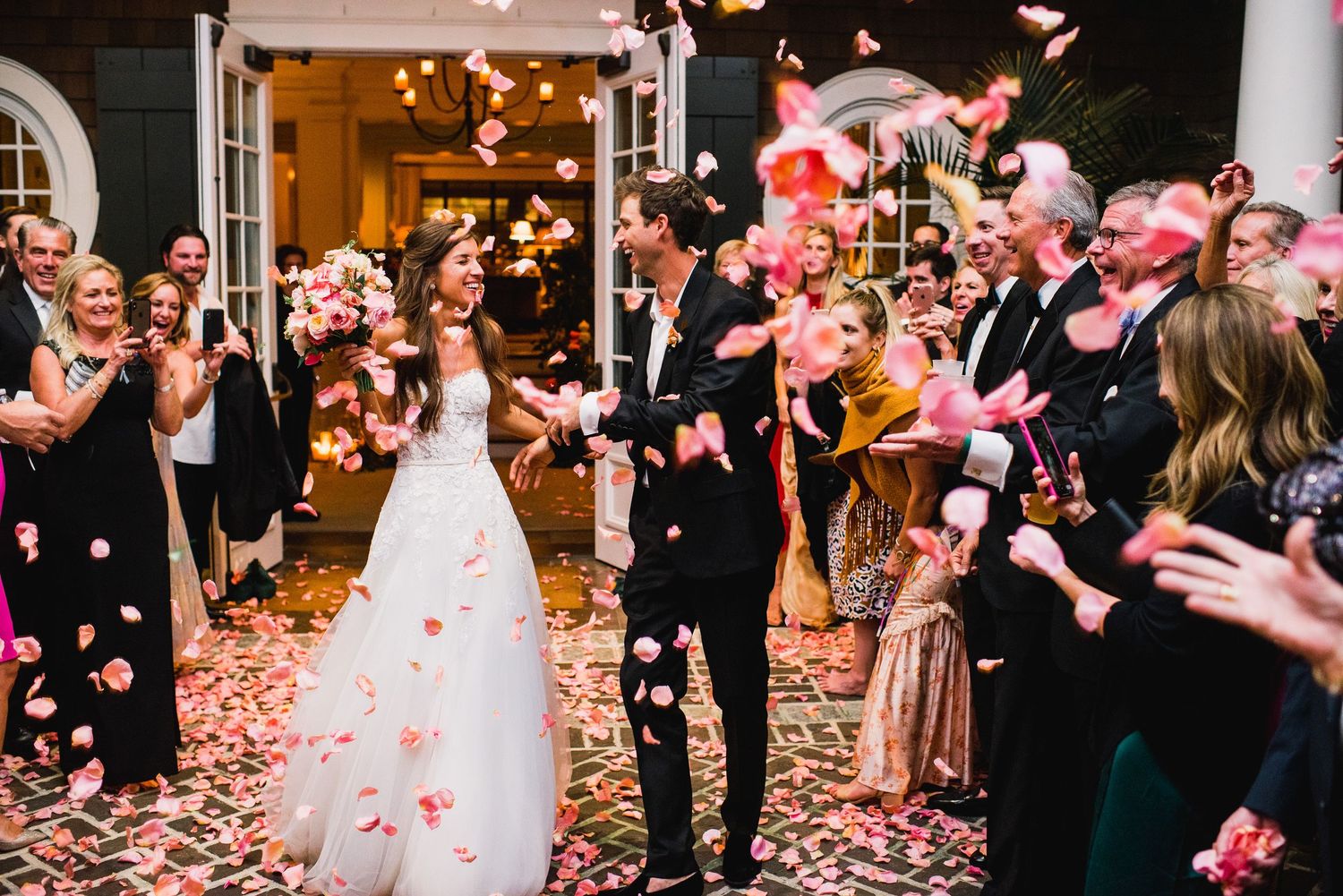Wedding guests shower newlyweds with pink rose petals during a joyful exit celebration at an elegant venue.