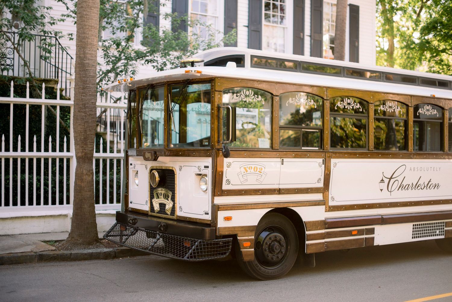 Row of white vintage tour buses parked outside a historic building with tall trees and columns.
