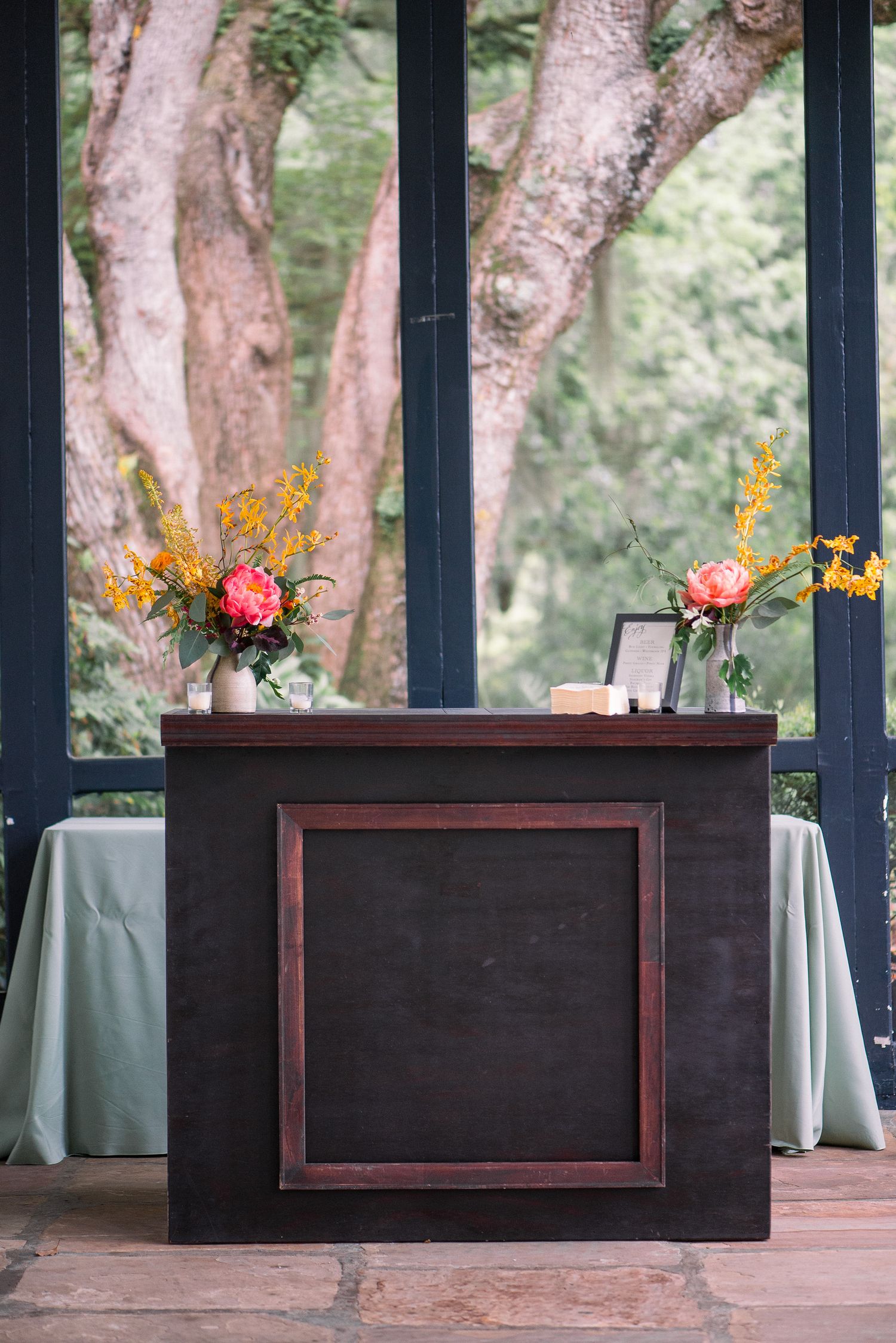Dark wooden bar tables decorated with small floral arrangements and sunflowers on an outdoor patio.