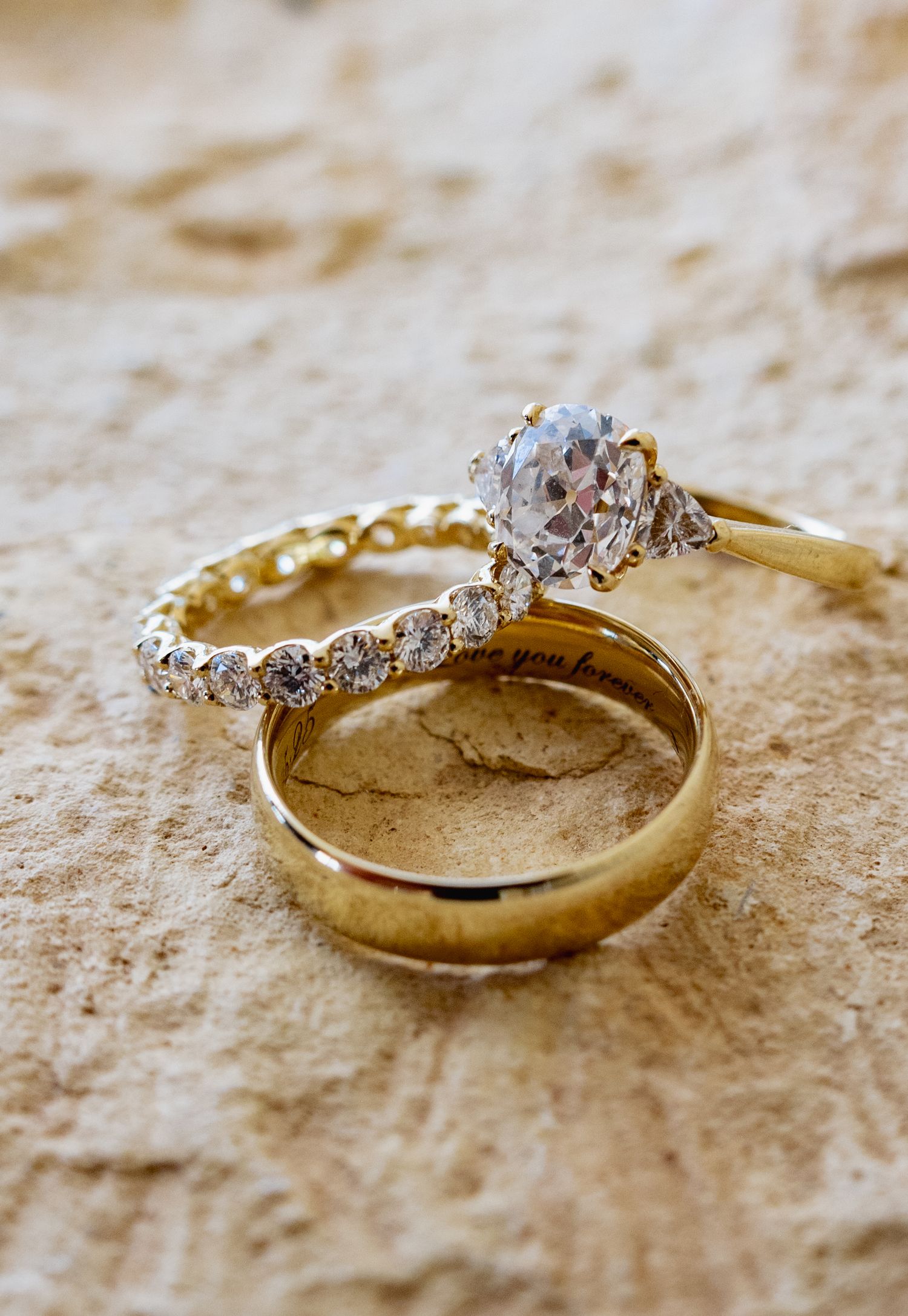 Gold wedding rings with diamond accents photographed on textured stone surface.
