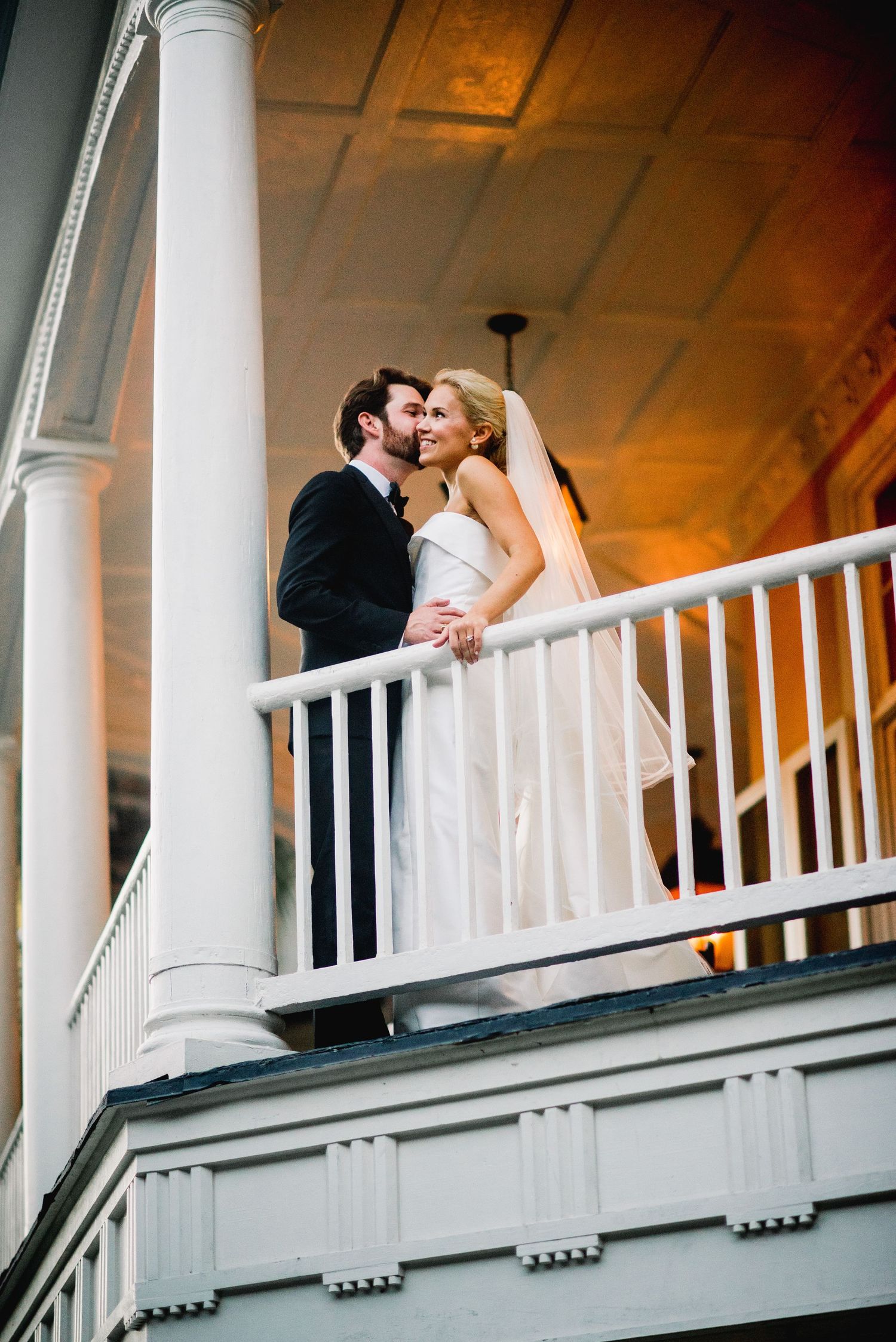 A romantic wedding couple shares a kiss on a white columned balcony in a sequence of progressive shots.
