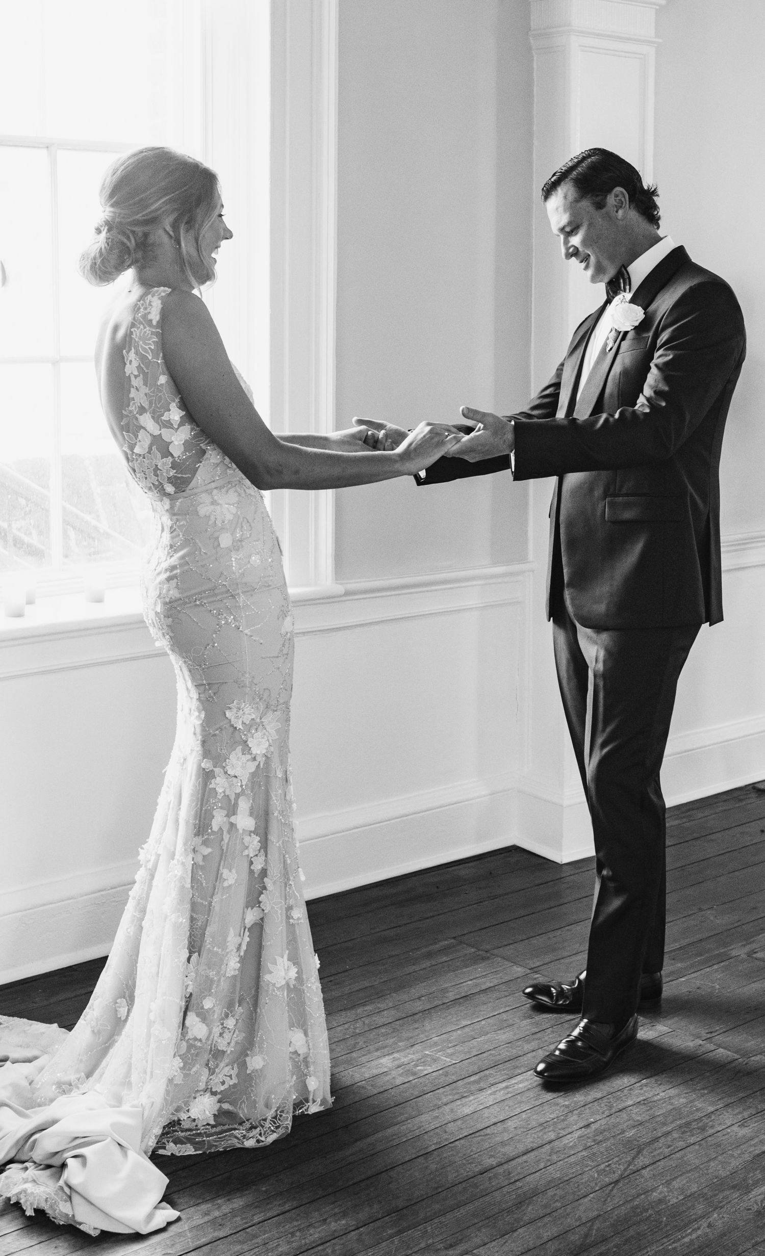 A tender first look moment between a couple in formal wedding attire in a bright indoor setting.