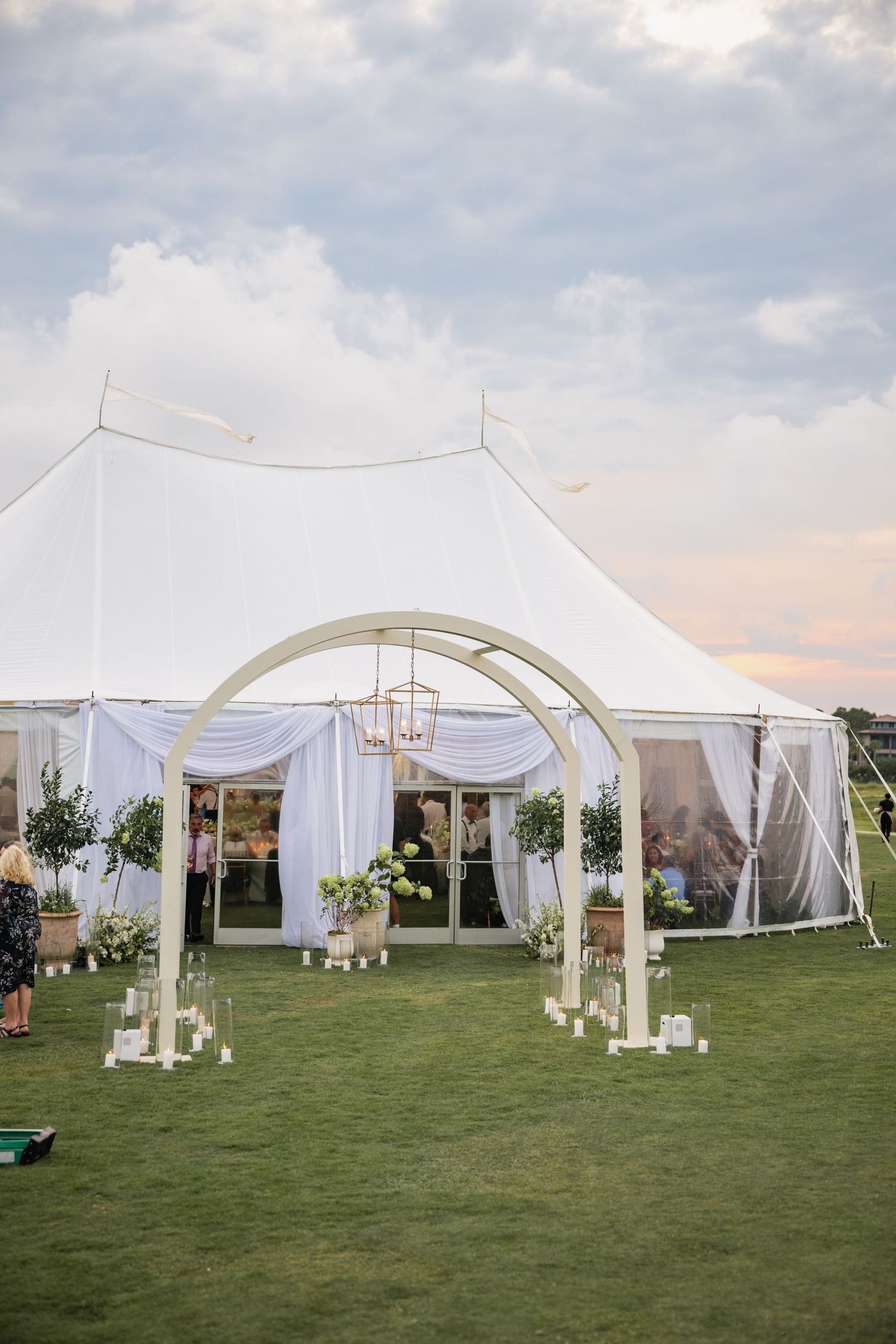Large white wedding tent setup on a green lawn with elegant draping and outdoor lighting.