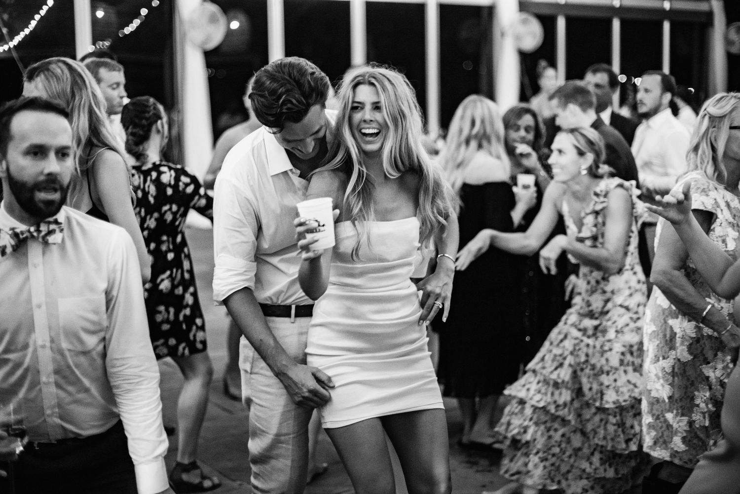 Black and white photo of wedding guests dancing and celebrating at a reception party.