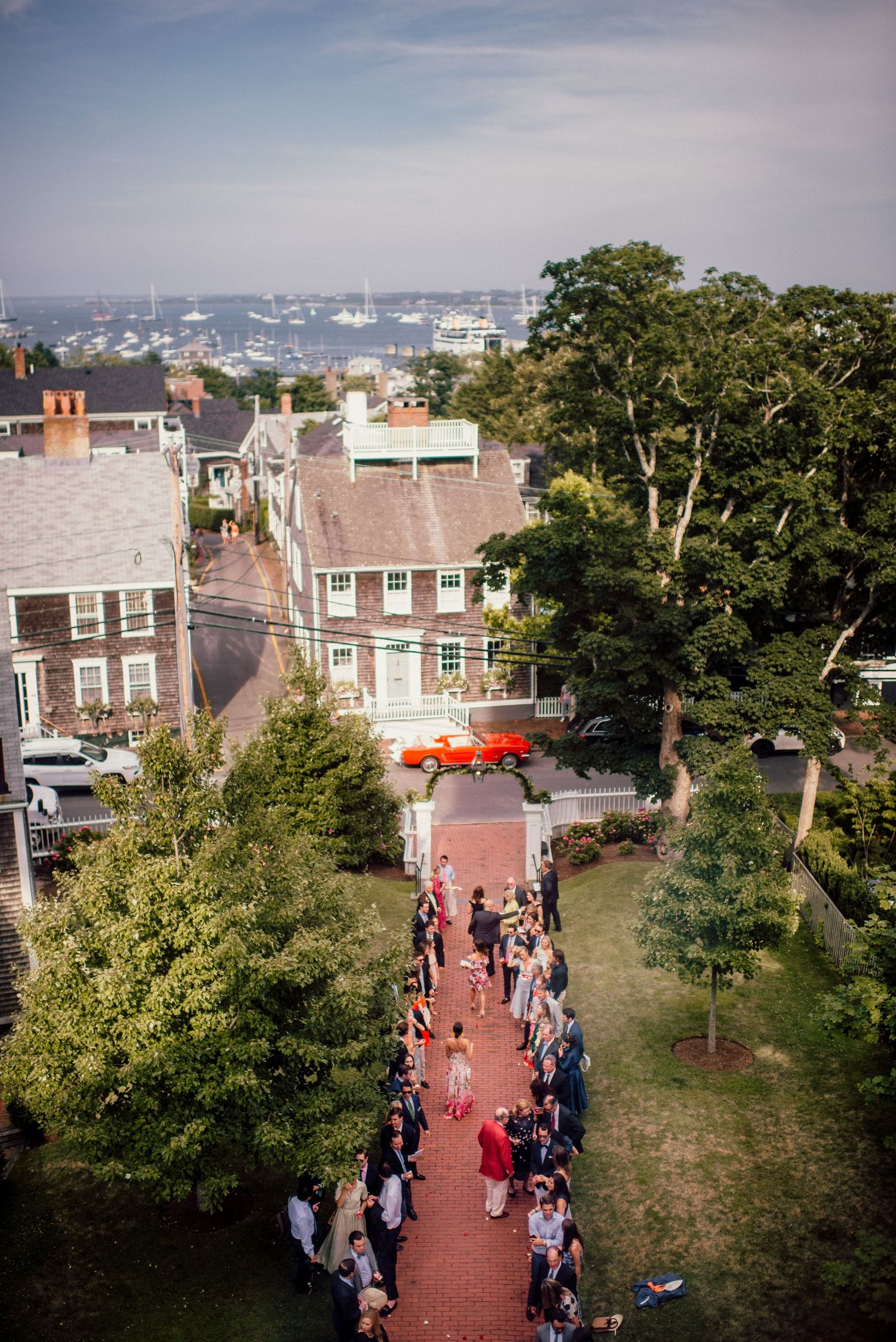 Aerial view of wedding guests lining brick pathway with harbor and boats visible in background.