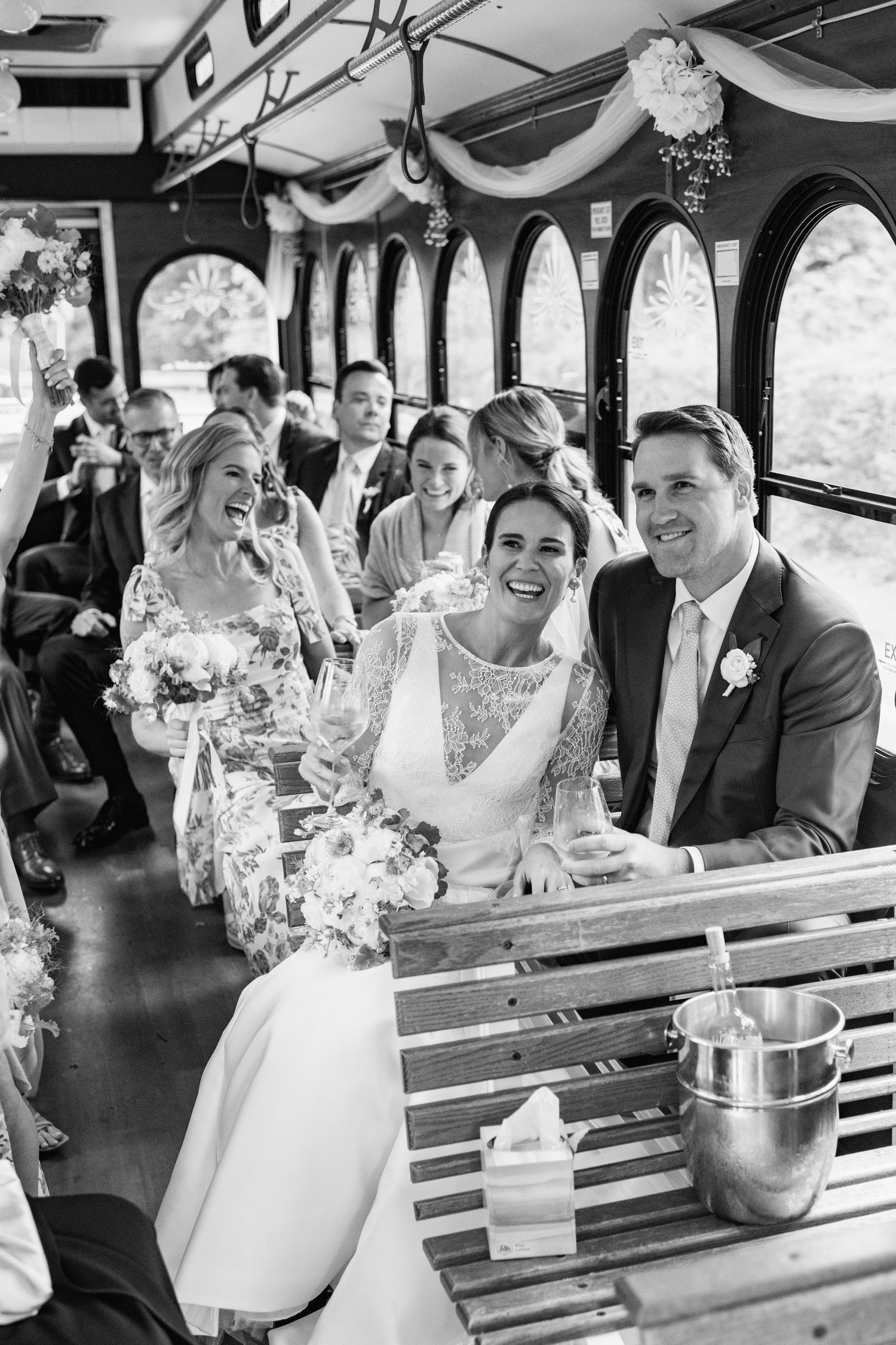Wedding party celebrates with champagne while riding in a vintage trolley decorated with white fabric swags.