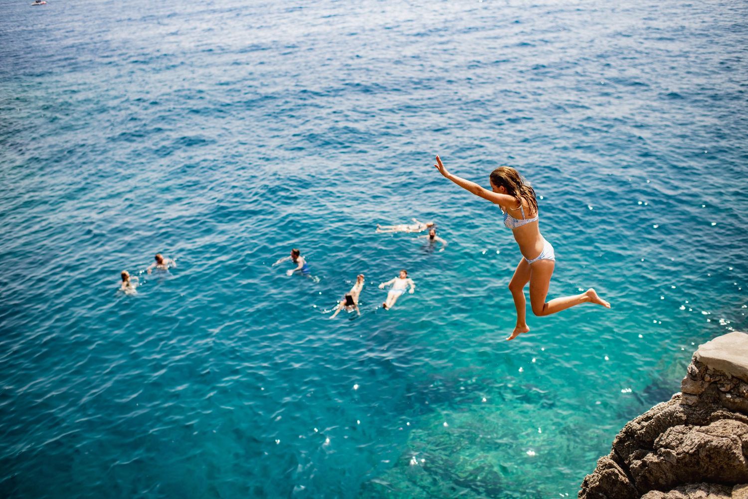 Cliff jumping into crystal clear turquoise Mediterranean waters of Amalfi Coast in Praiano on a sunny summer day.