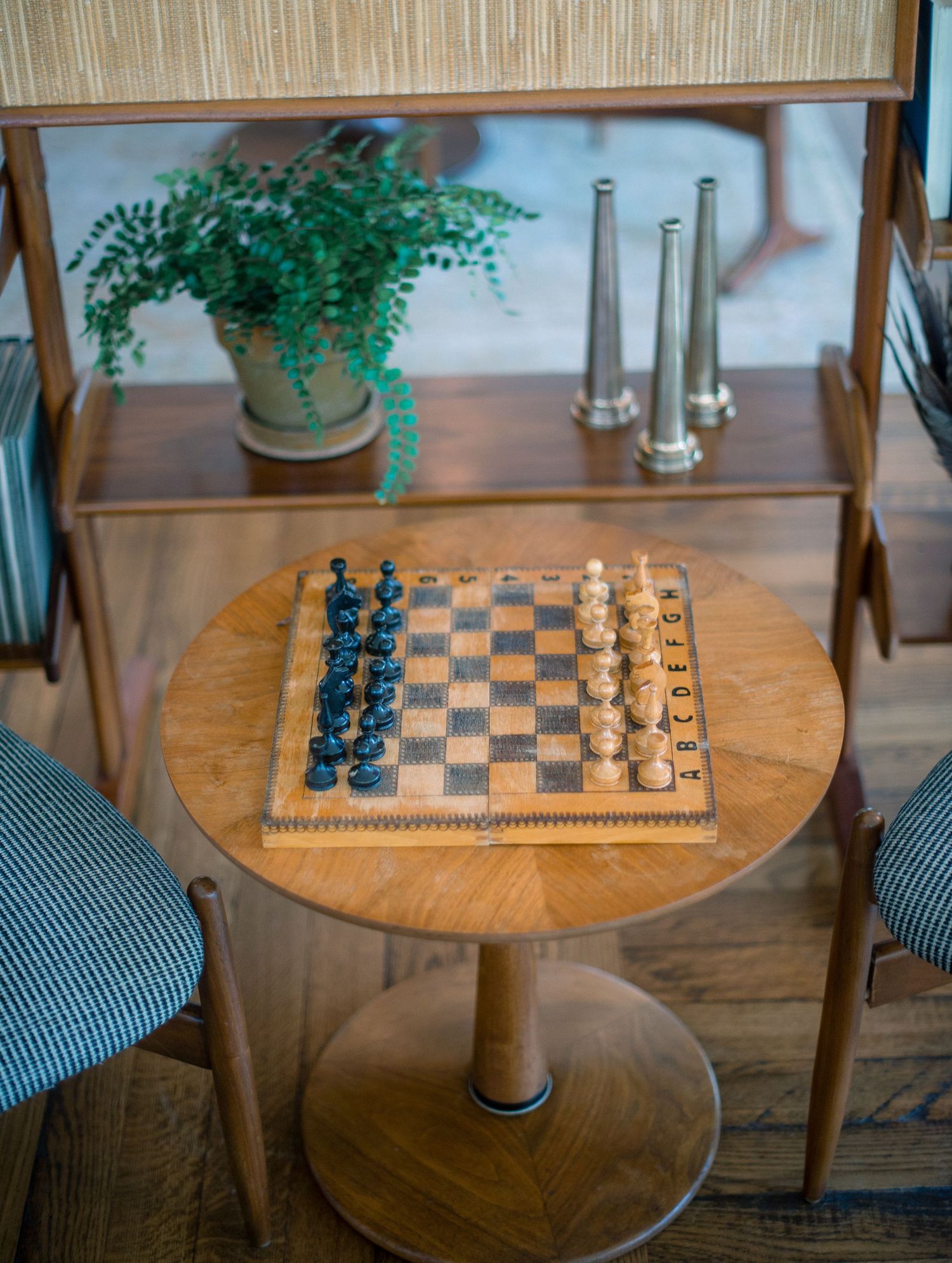 A wooden round chess table with black and white pieces set up for a game in a cozy interior space.