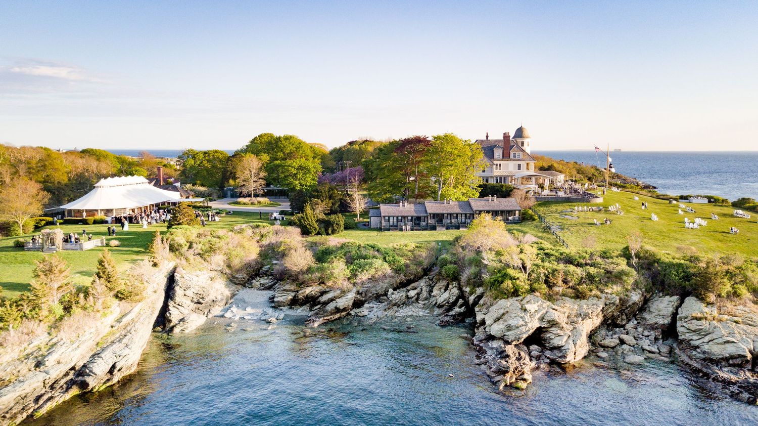 Aerial panoramic view of rocky coastline with blue ocean waters and green vegetation along cliffs in summer.