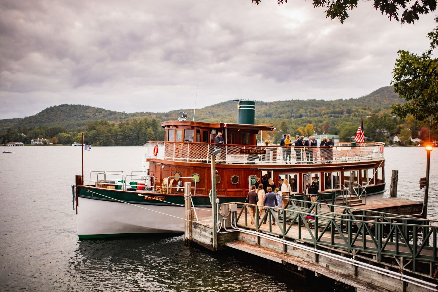 Rustic lakeside dock with wooden boat house and mountains in the background on a cloudy day.