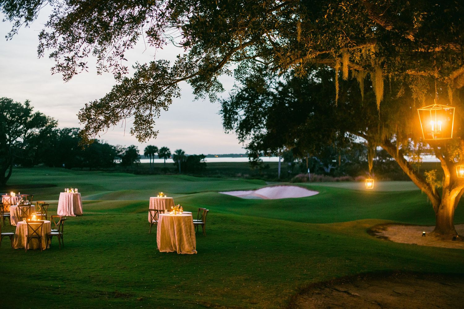 Elegant outdoor wedding reception setup at dusk with string lights illuminating tables on a golf course.