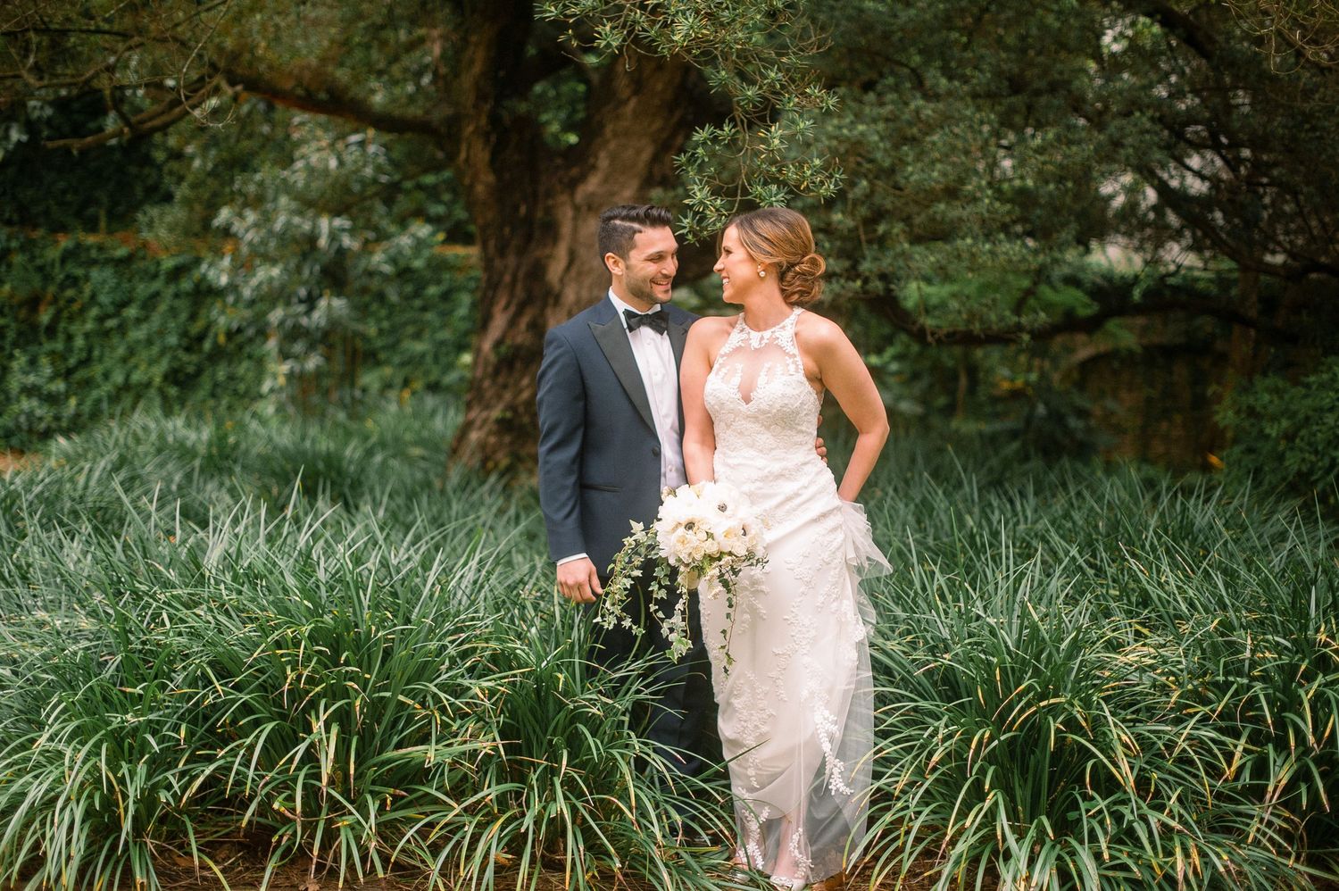 A couple shares a romantic moment in a lush garden setting with tall ornamental grasses and greenery.