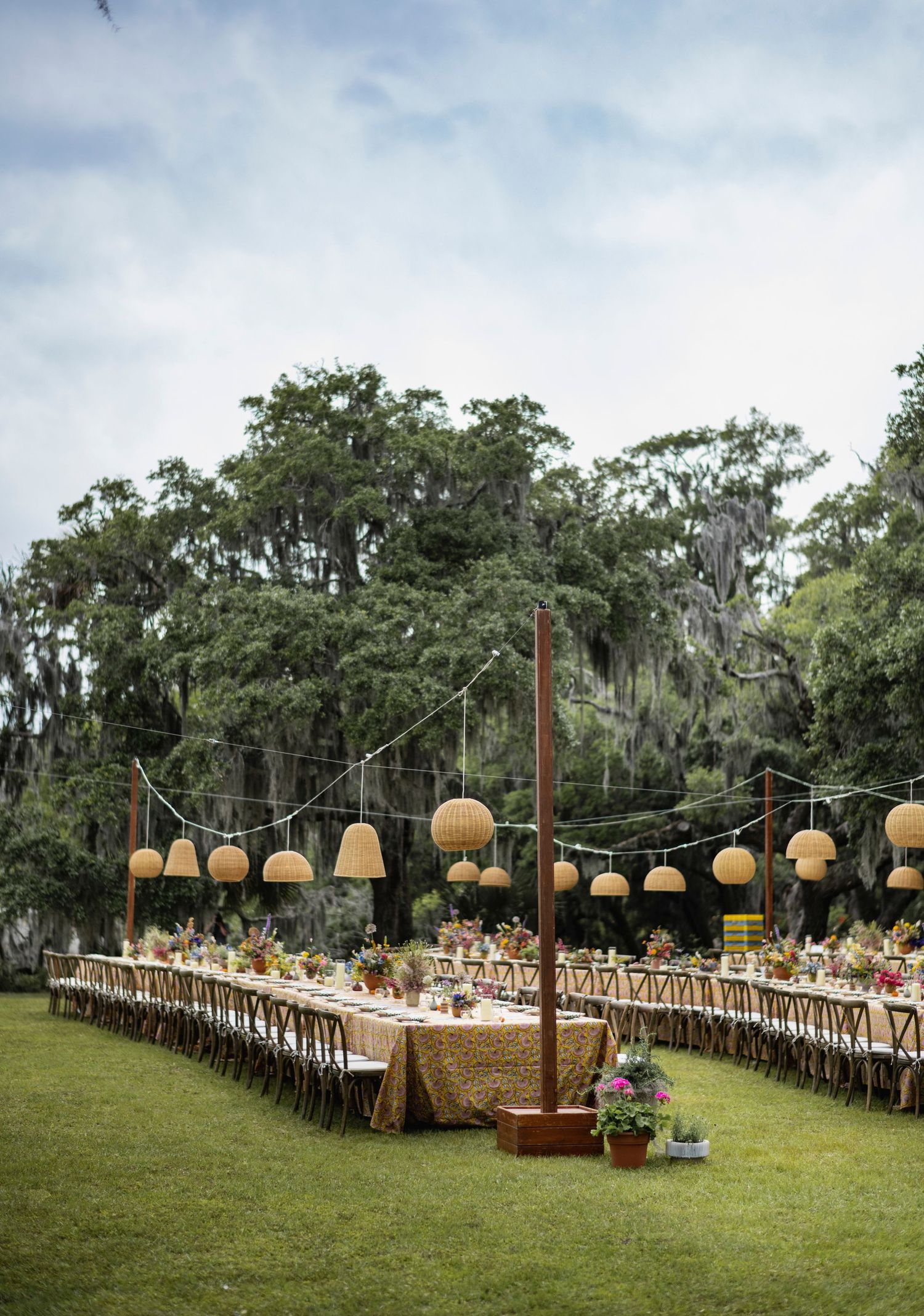 Long banquet tables decorated with lanterns and floral arrangements create an elegant outdoor wedding reception setting.