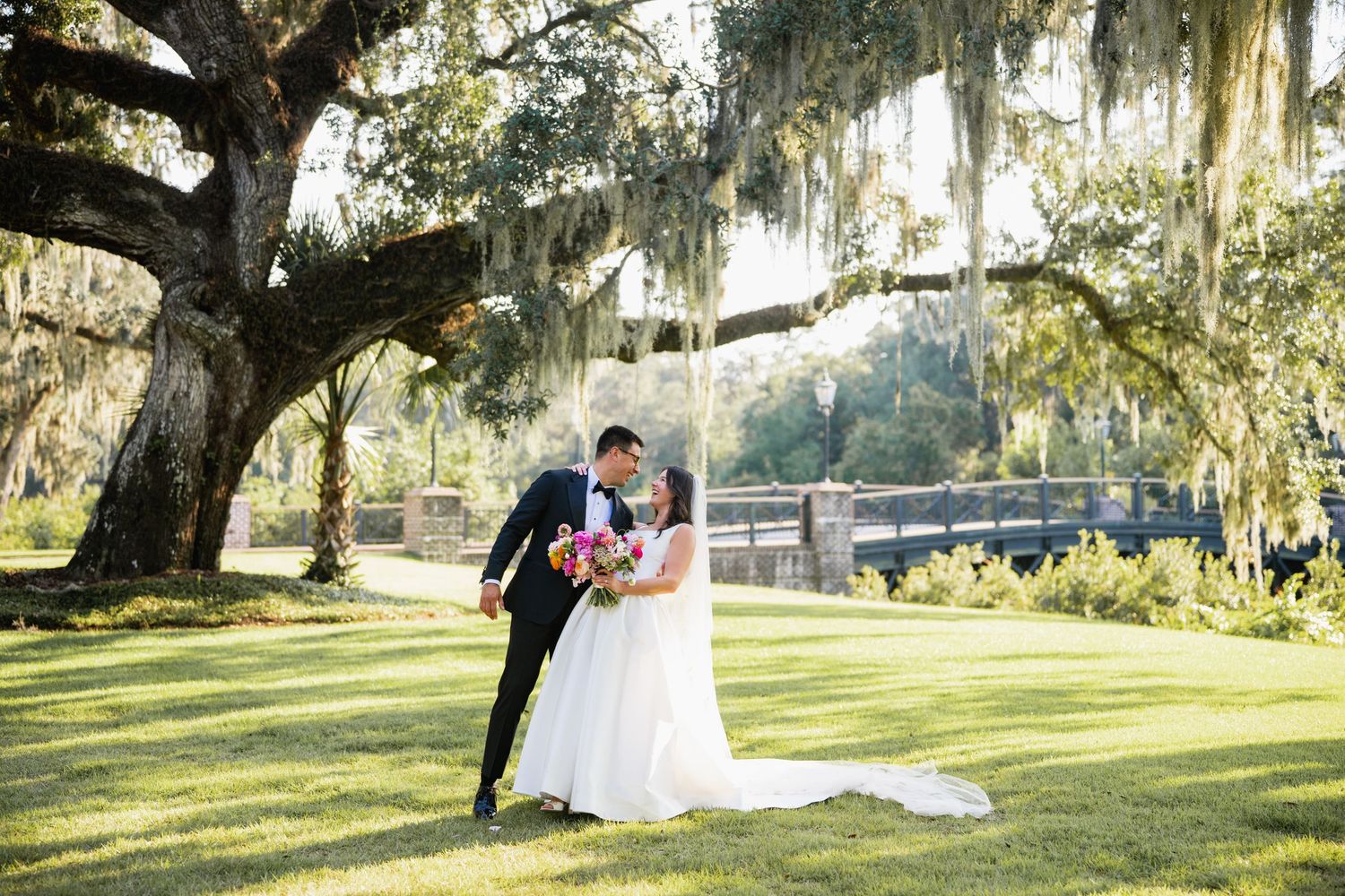 A couple shares a romantic moment under Spanish moss draped oak trees in a scenic outdoor setting.
