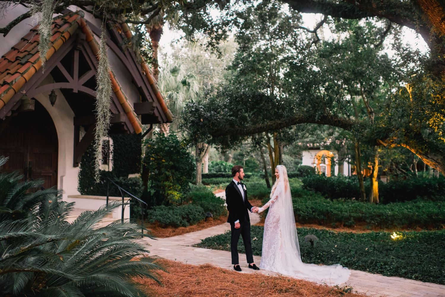 A couple walks together through a scenic garden pathway during a wedding photo session at sunset.