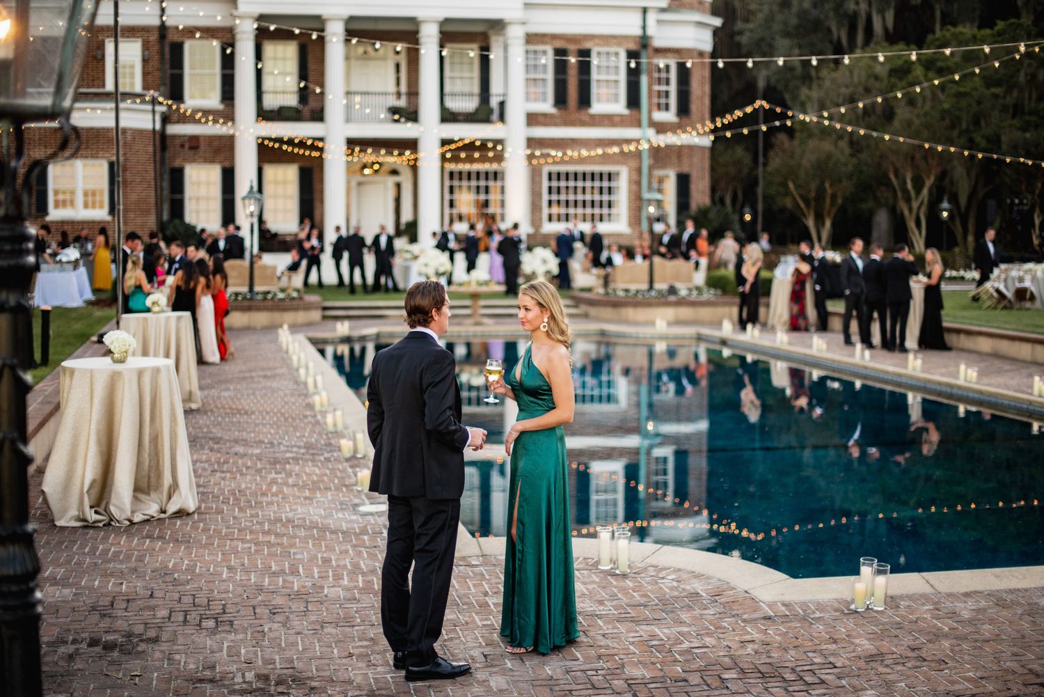 Wedding guests mingle and dance on an outdoor patio decorated with string lights during an evening reception.