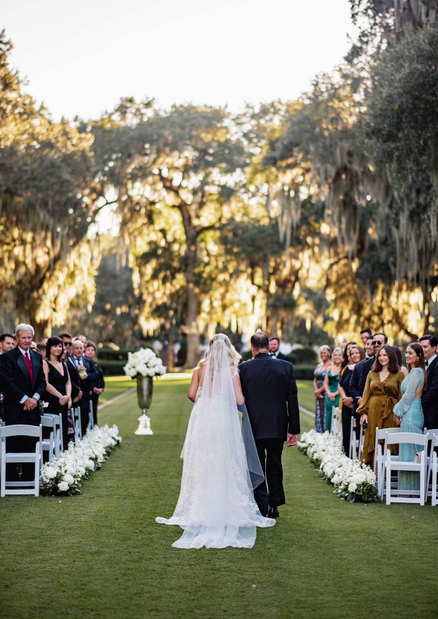 Outdoor wedding ceremony on a lush green lawn with Spanish moss draped trees at sunset.