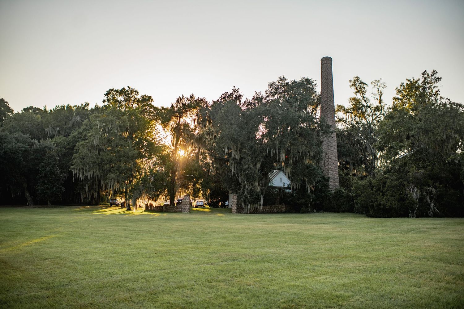 Scenic sunset view of a grassy field with trees and a church steeple silhouetted in the background.