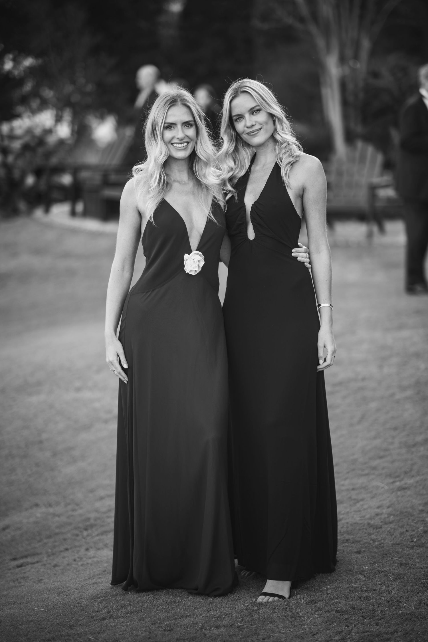 Two women in matching black formal maxi dresses pose together outdoors in black and white photography.