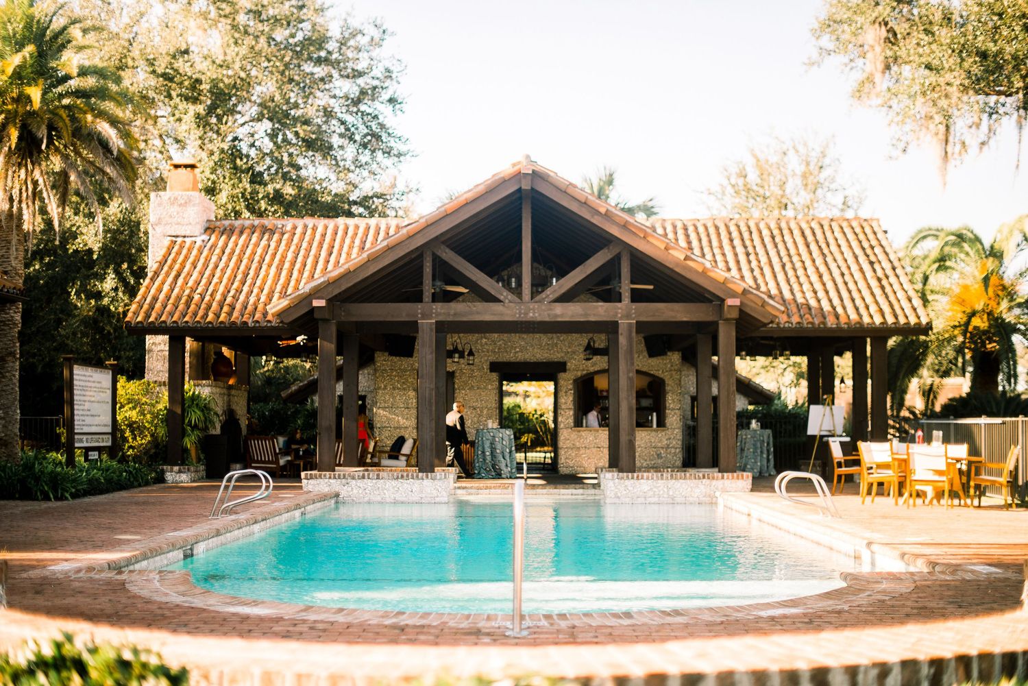 Panoramic view of a luxury resort pool area with Spanish-style architecture and palm trees at sunset.