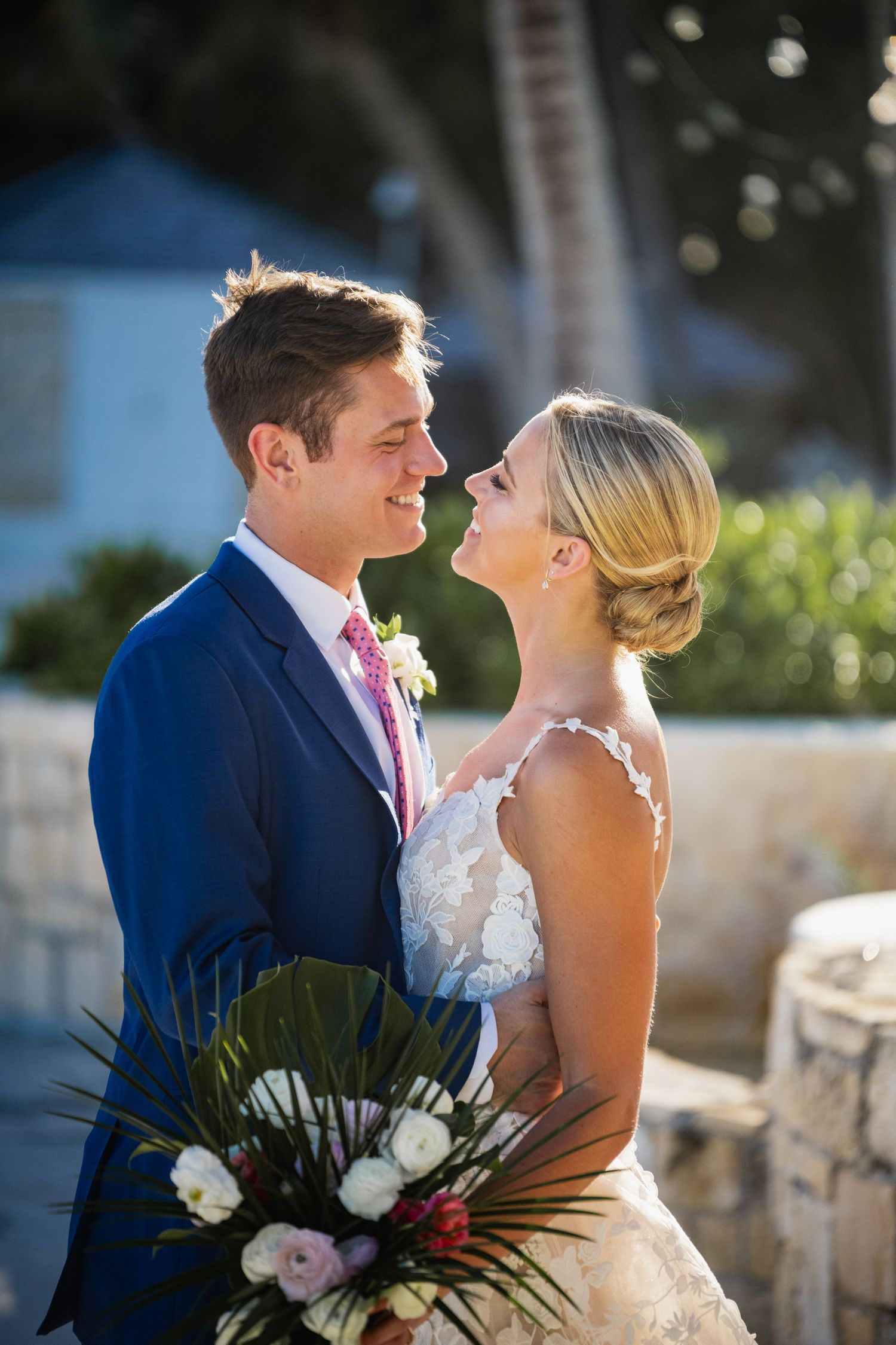 A romantic wedding portrait captured in beautiful natural sunlight with tropical foliage in the background.