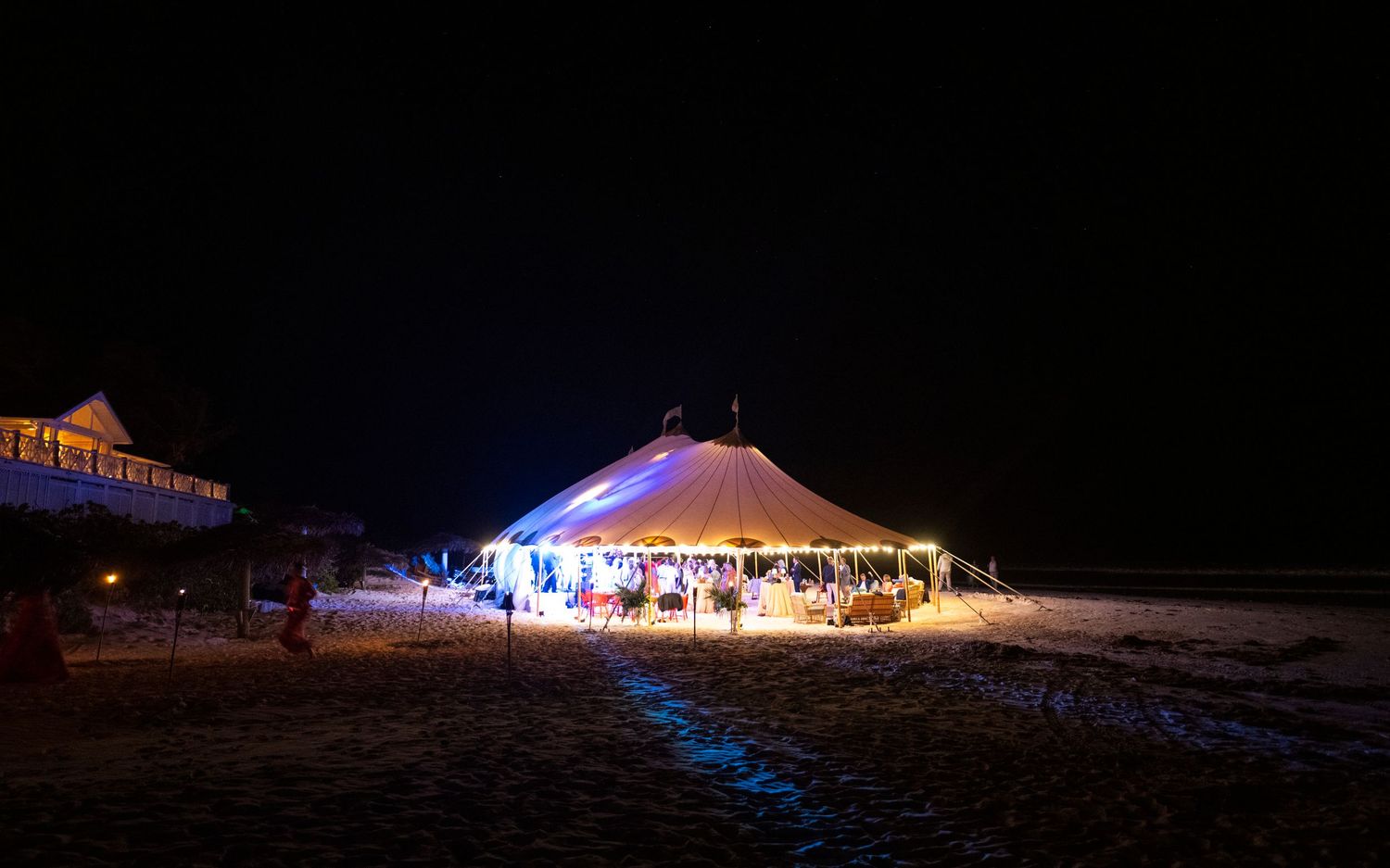 A large illuminated white tent glows at night in a snowy field with blue lighting accents around its perimeter.