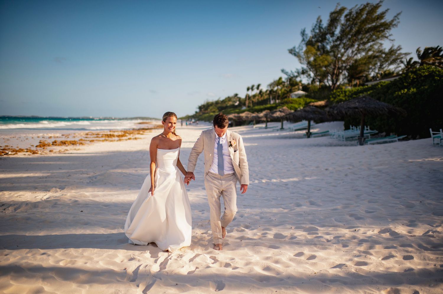 People walking along a pristine white sand beach with palm trees and ocean views.