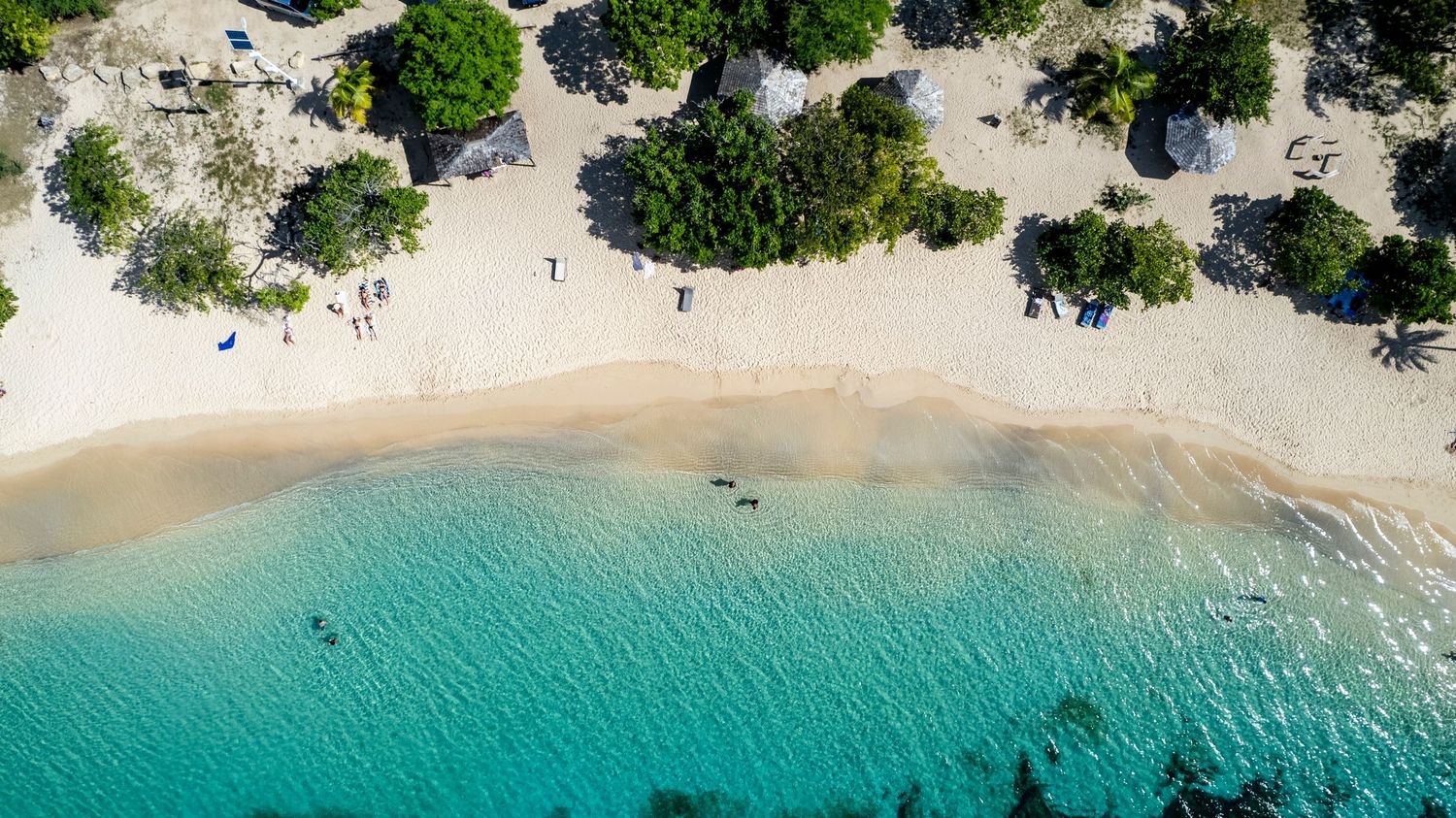 Aerial panorama of a pristine white sand beach with turquoise waters and lush greenery.