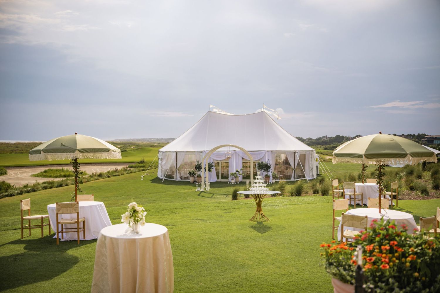 White wedding tent pavilion set up on rolling green hills with elegant floral arrangements.