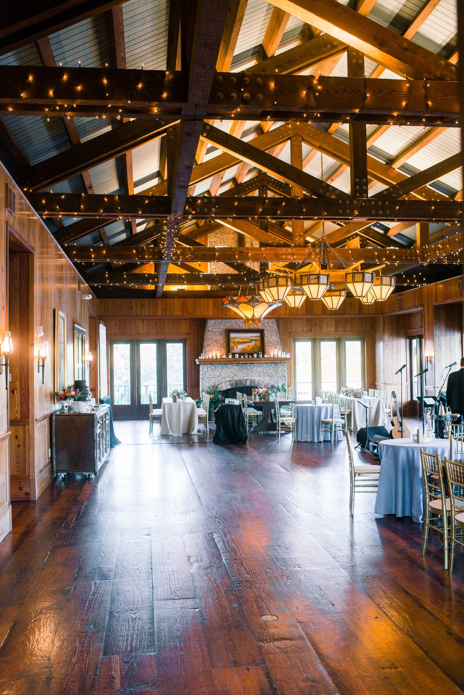 Rustic wooden event venue interior with exposed beams, string lights, and hardwood floors for a wedding reception.
