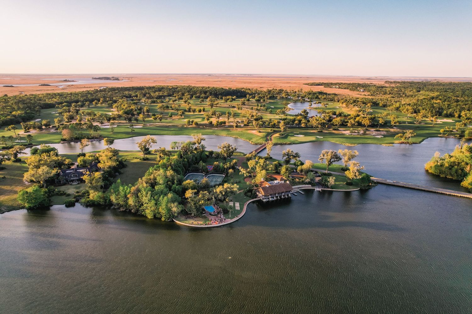 Aerial view of luxury lakefront homes and docks nestled among trees on a scenic waterfront peninsula during sunset.