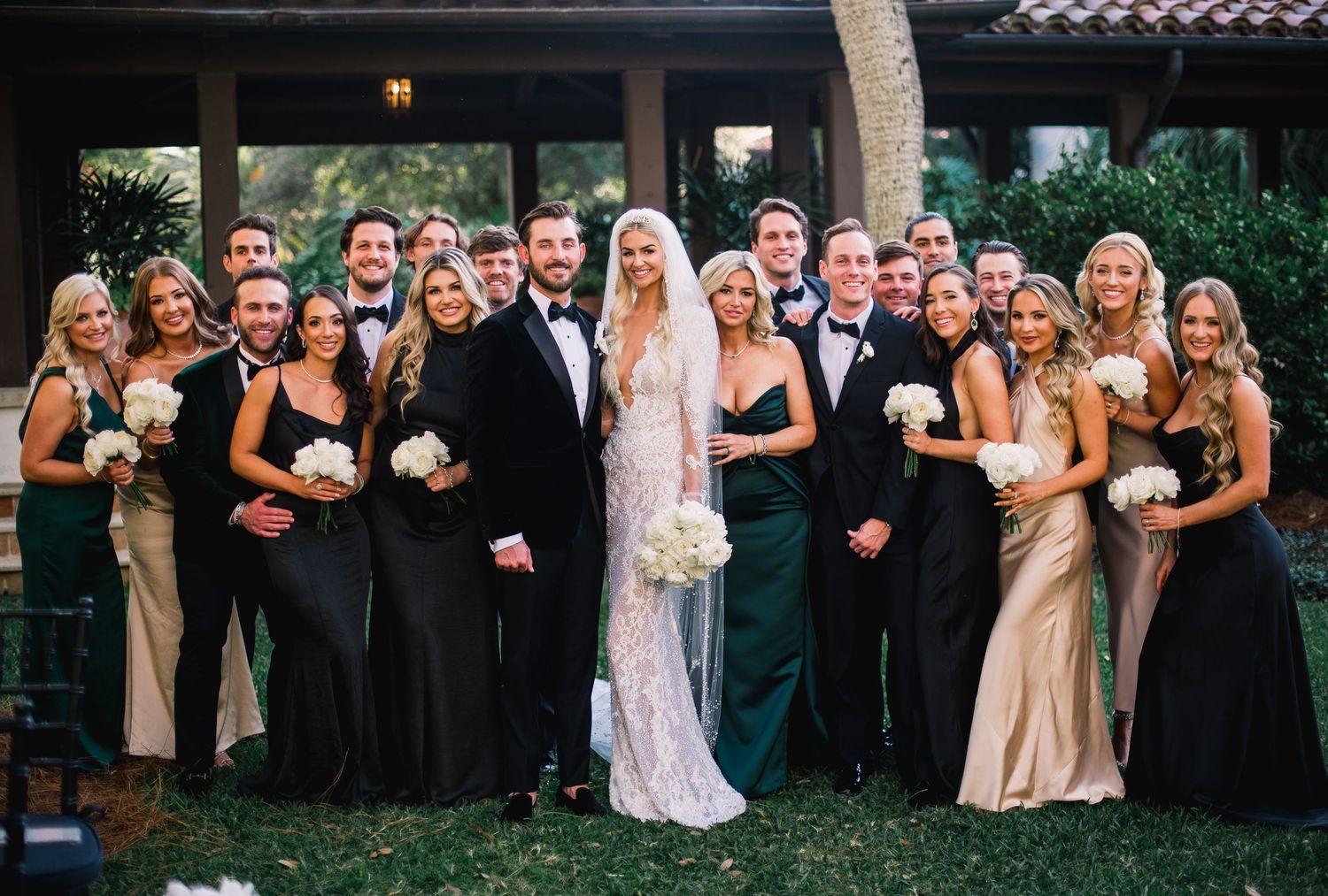 Wedding party in formal attire poses together outdoors in a line formation at sunset.