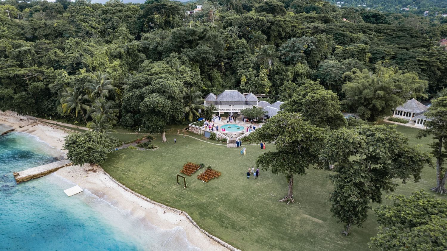 Panoramic aerial view of a luxury beachfront villa with lush tropical gardens and private dock in the Caribbean.