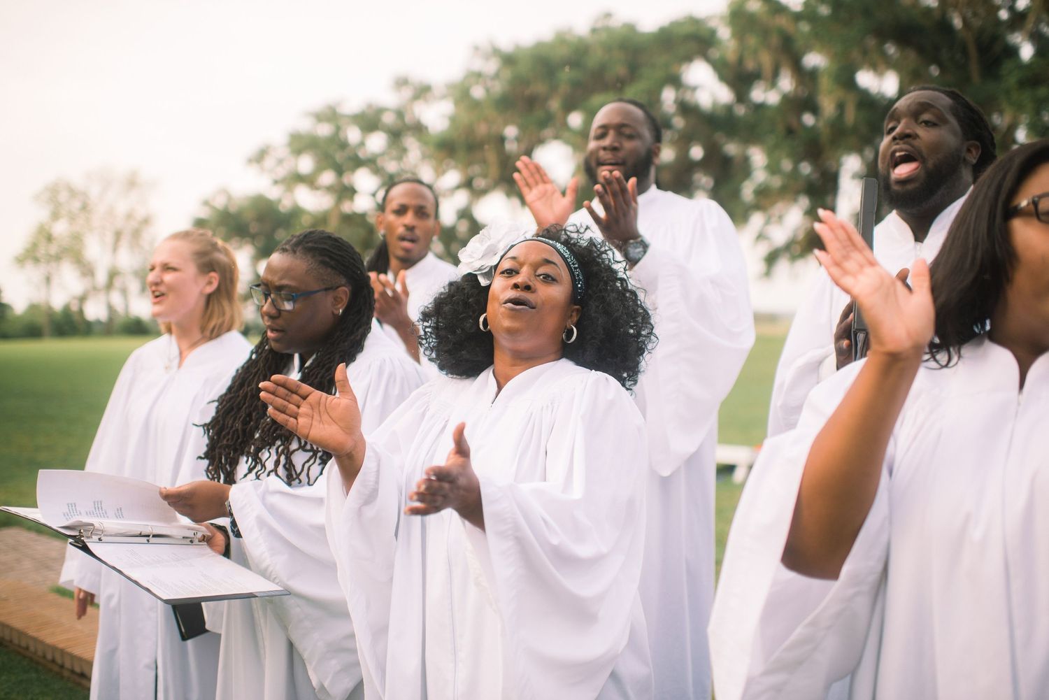 A joyful gospel choir wearing white robes performs together with passionate expressions during a musical performance.