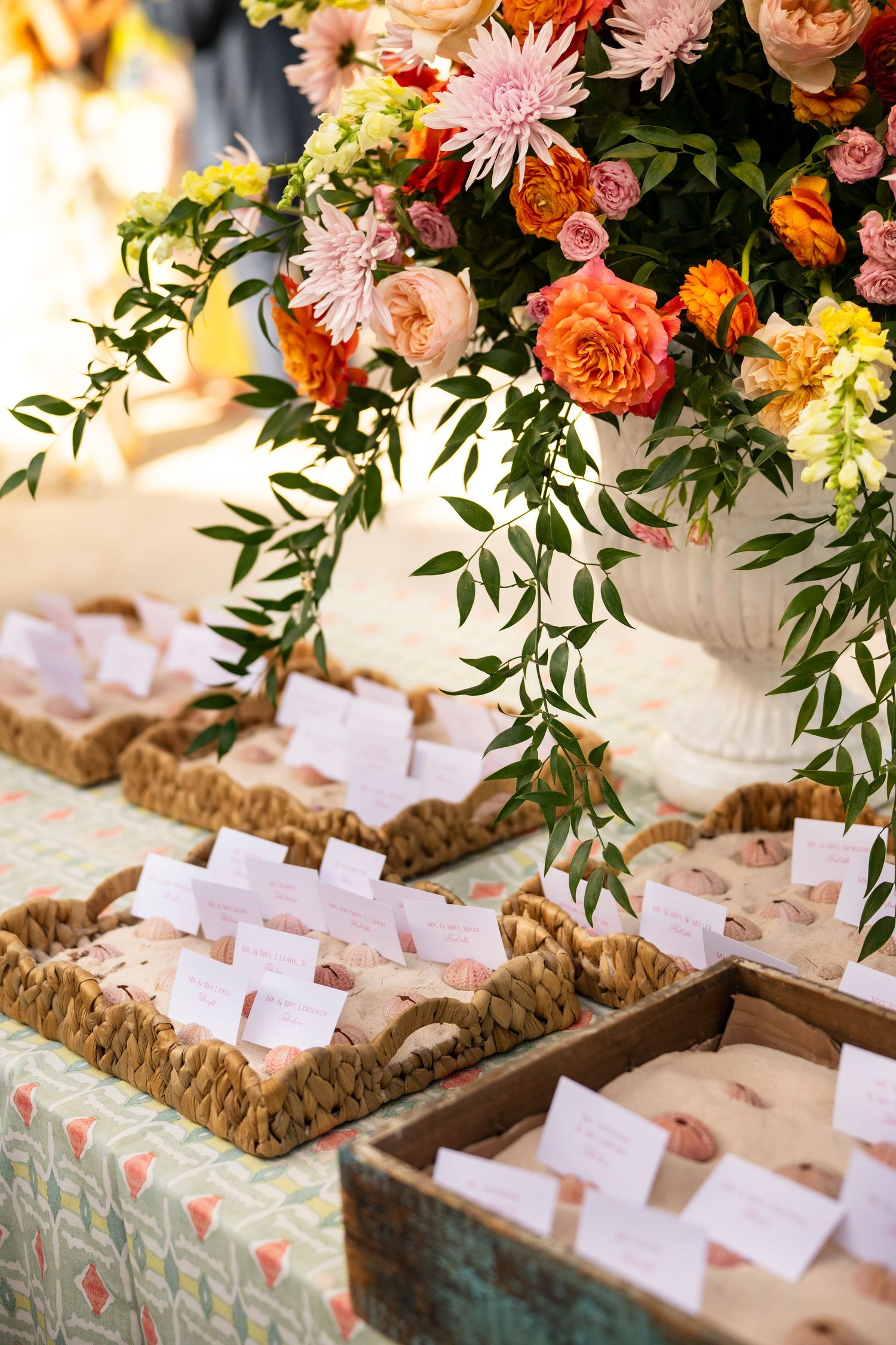 Wedding place cards displayed on rustic wood slices with coral and peach floral arrangements and greenery above.