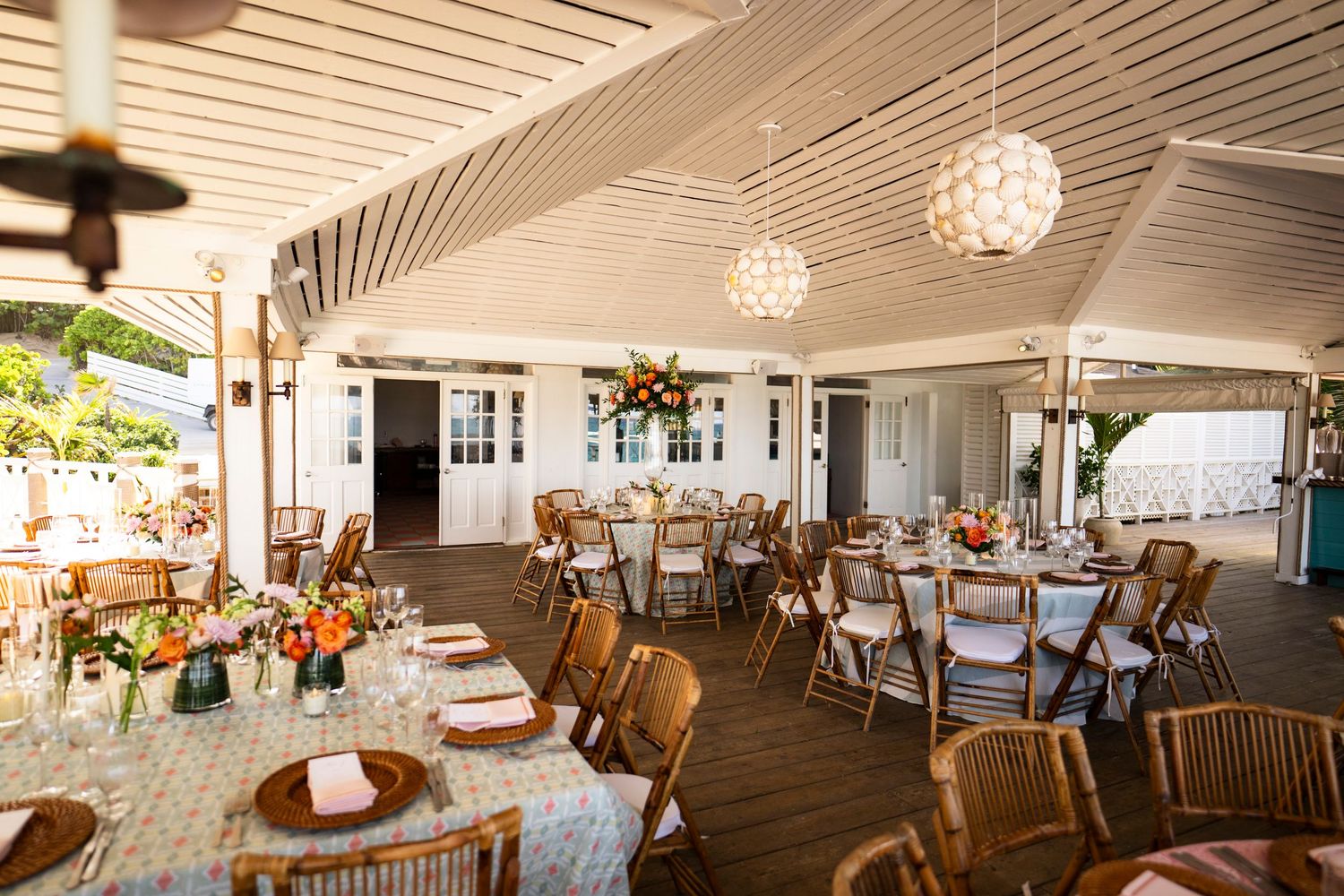 Elegant wedding reception venue with round tables, wooden chairs and hanging crystal light fixtures on a covered deck.