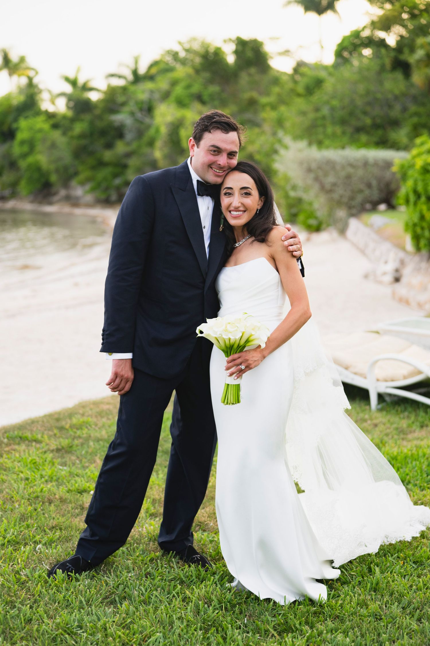 A happy couple in wedding attire shares a joyful moment together on green grass outdoors.