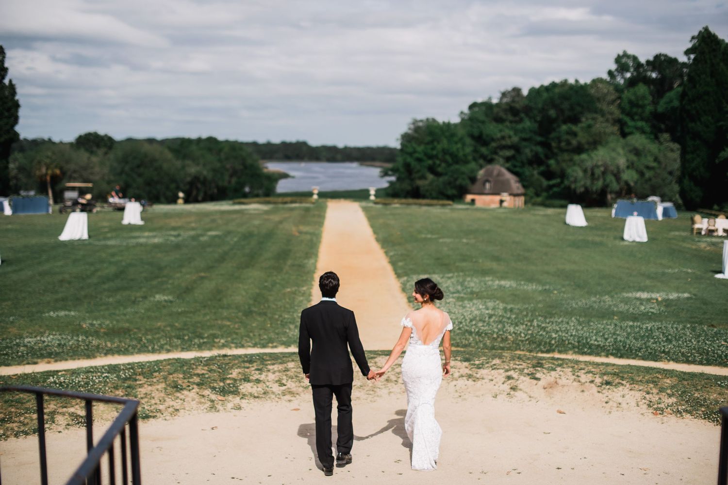 Wedding couple strolling along a scenic waterfront path surrounded by lush greenery.