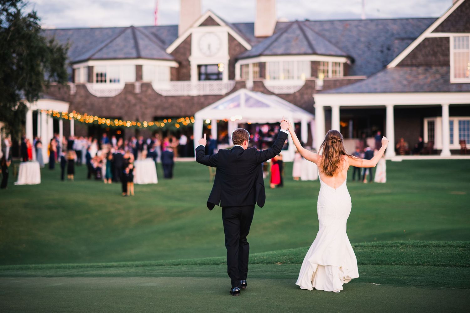 A couple walks together on a lush green golf course during an outdoor wedding celebration.