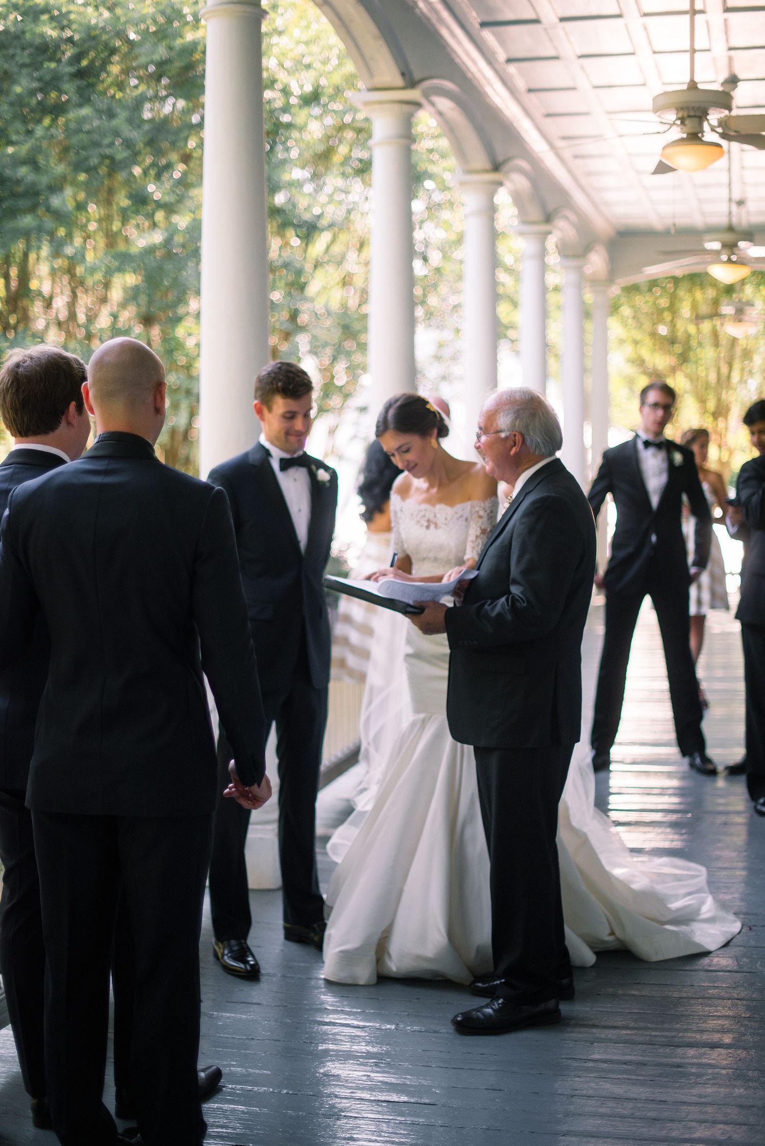 Wedding party gathers on an elegant columned porch with black and white formal attire during an outdoor celebration.