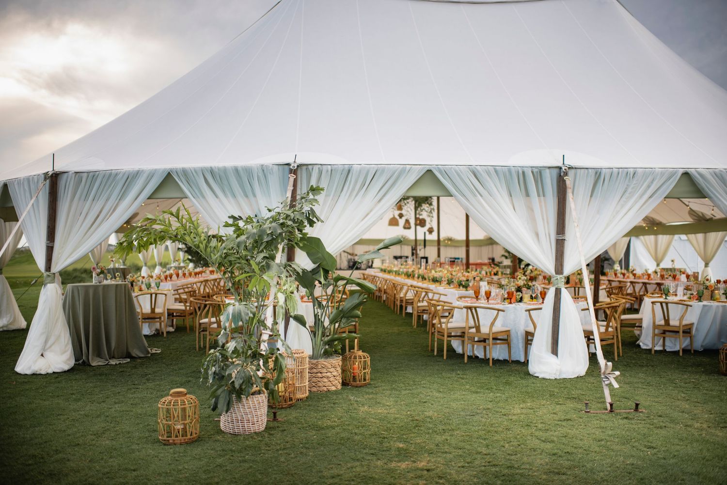 White wedding reception tents set up on a lush green lawn with elegant table settings and decor.