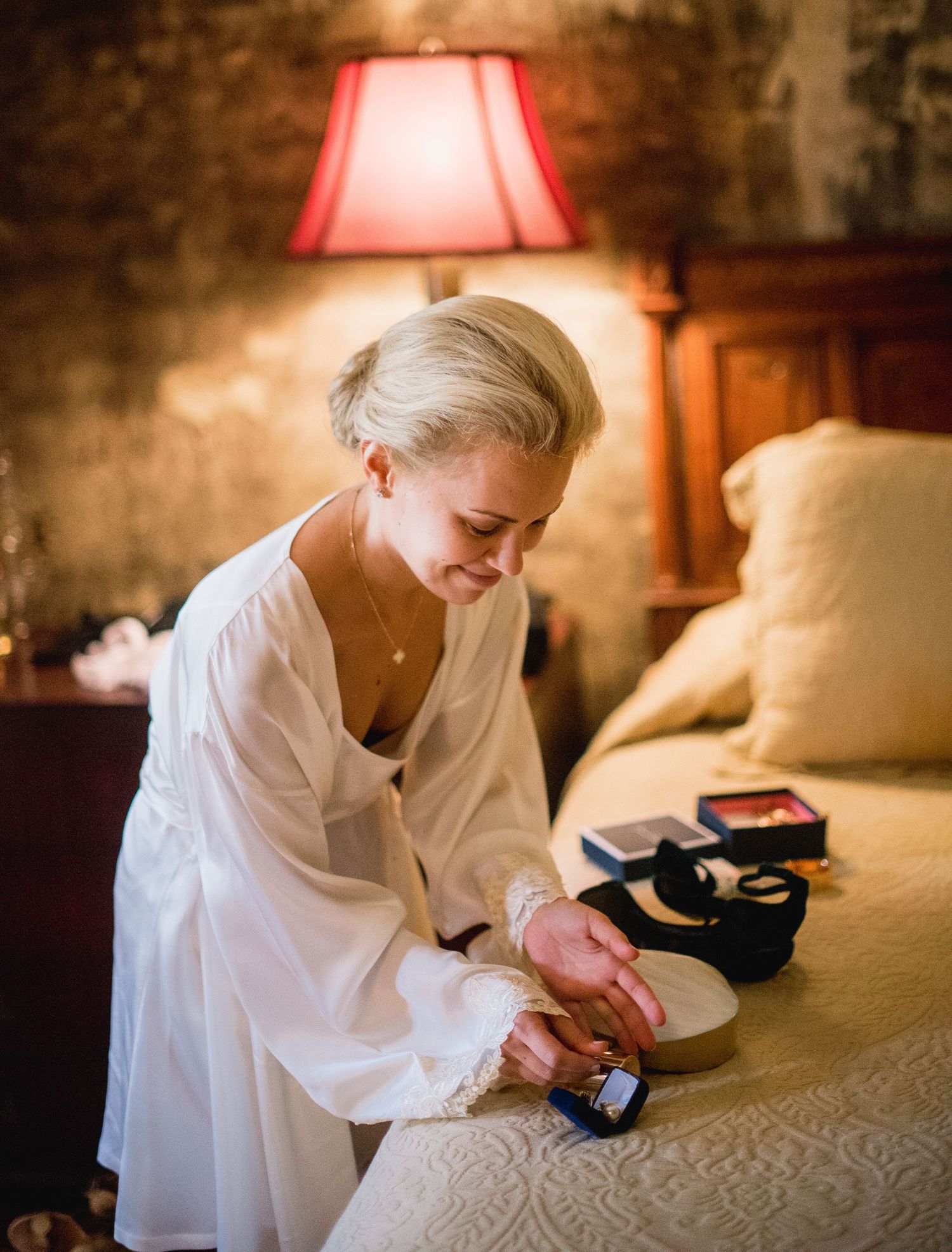Person in white robe sitting on bed while getting ready in warm, cozy lighting with bedside lamp.