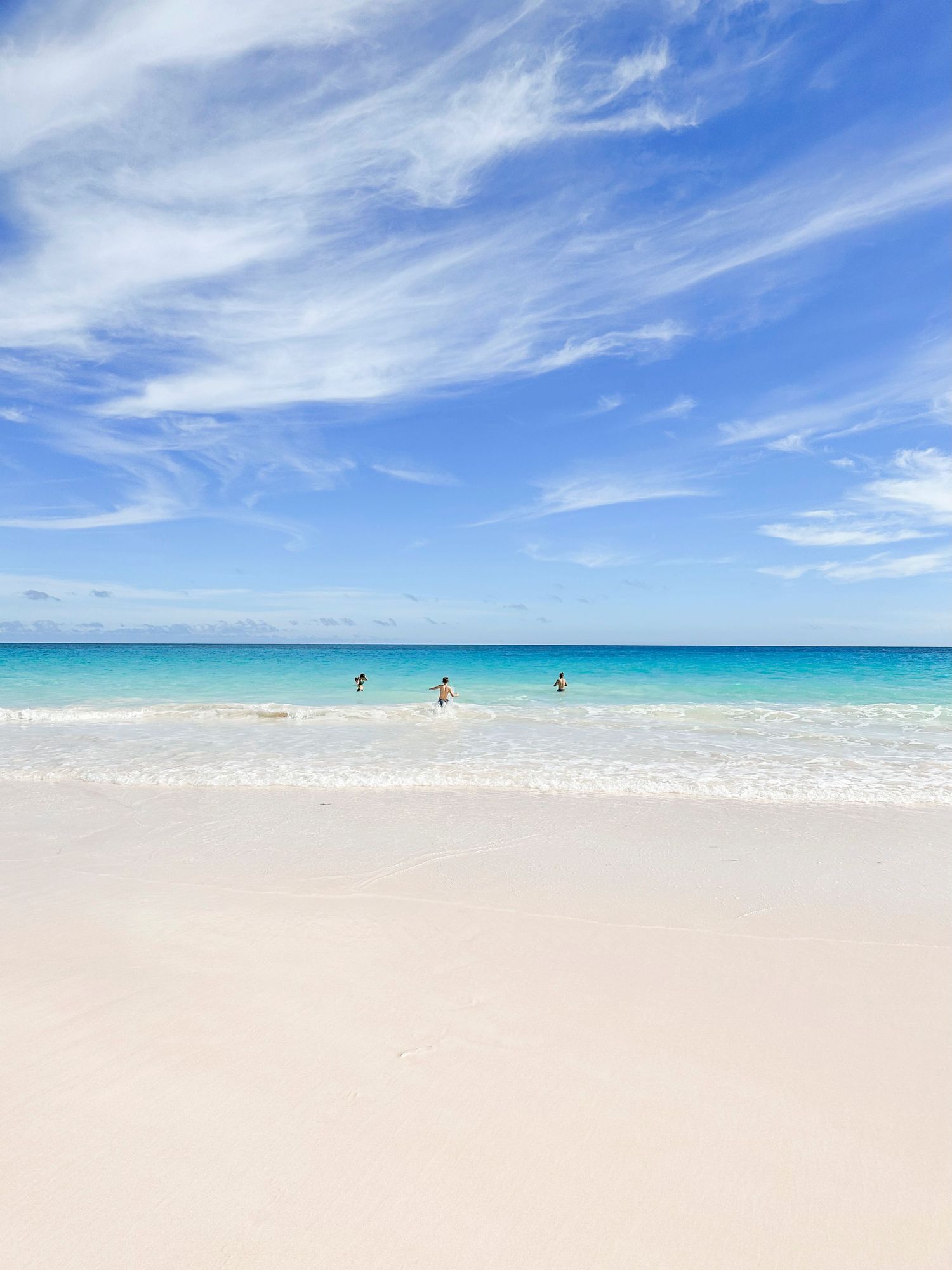 Pristine white sand beach with turquoise waters and wispy clouds in a bright blue sky.