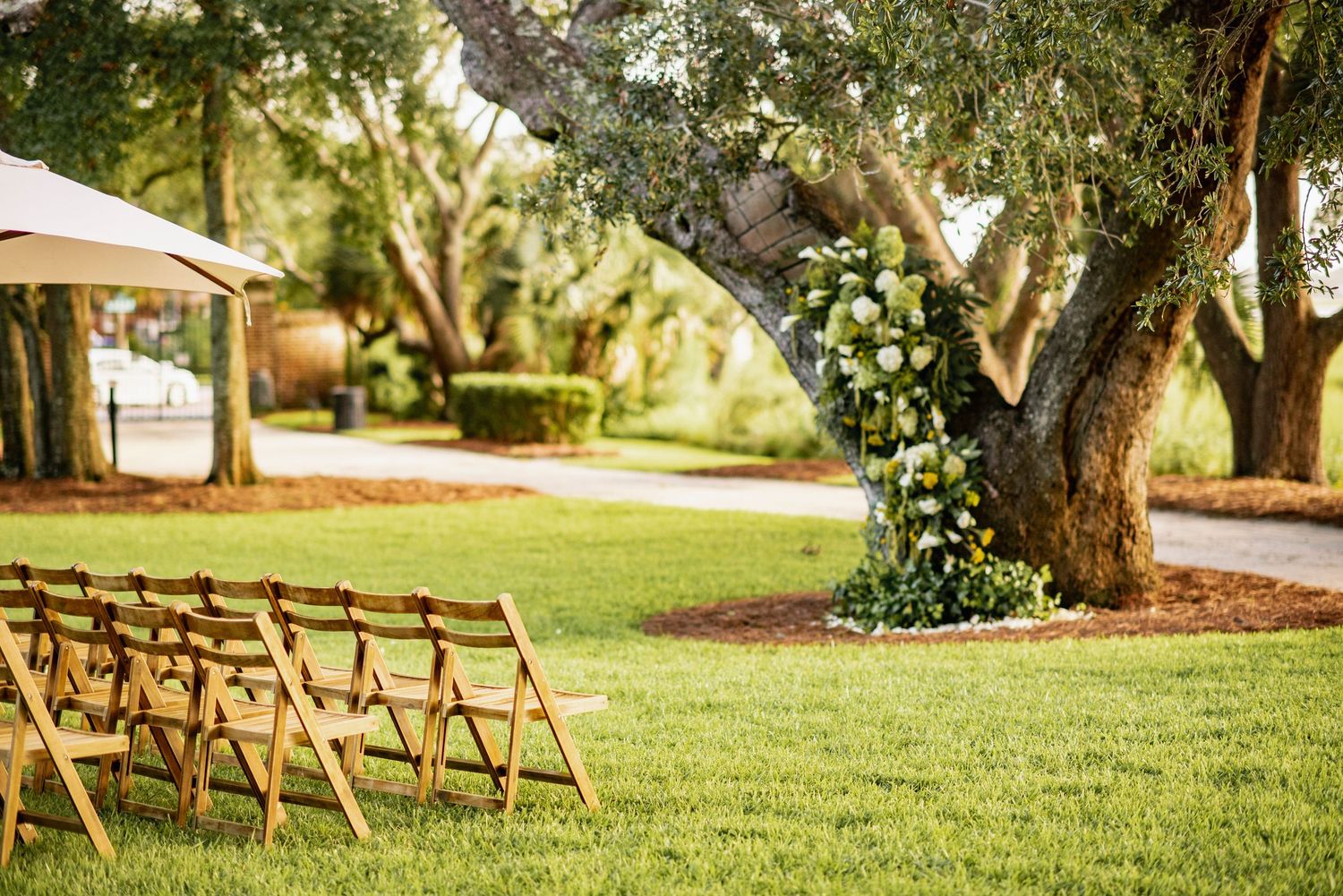Wooden folding chairs arranged on a green lawn for an outdoor wedding ceremony under shady trees.
